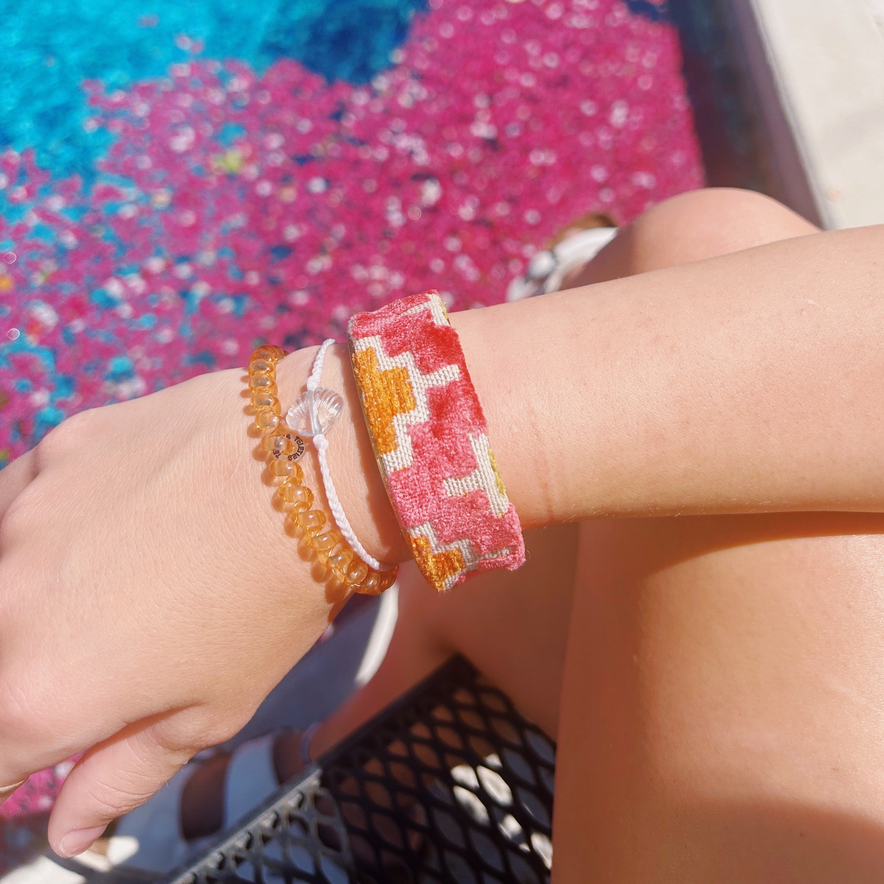 model wearing An open-back view of the Theta cuff showing its raw brass interior and velvet exterior with coral and mustard zigzag patterns on neutral linen, placed on a white surface.