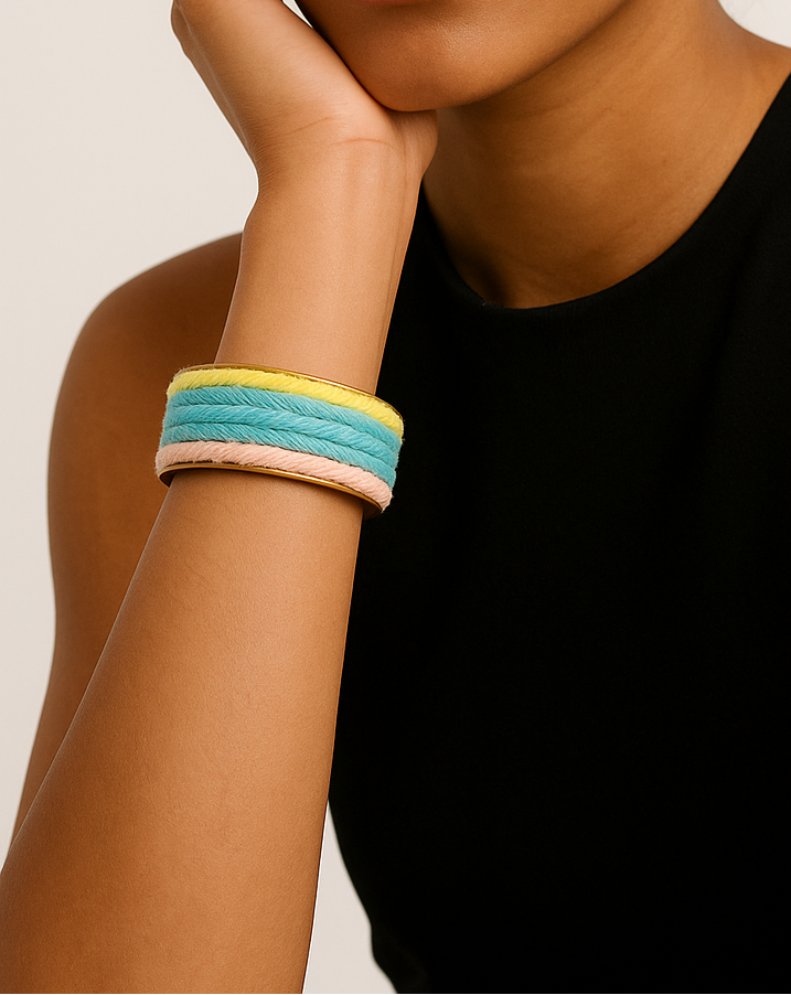 A female model wearing a one of a kind jewelry brass cuff bracelet for women—a 1-inch wide, open-back design wrapped in pastel mint, peach, and lemon yarn stripes, showcased on her wrist against a neutral background.