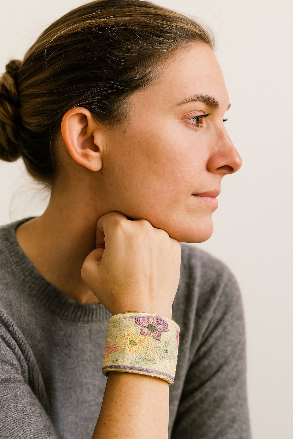 A female model wearing a one of a kind jewelry brass cuff bracelet for women—an open-back design wrapped in cream fabric with yellow and purple floral embroidery, showcased on her wrist against a neutral backdrop.