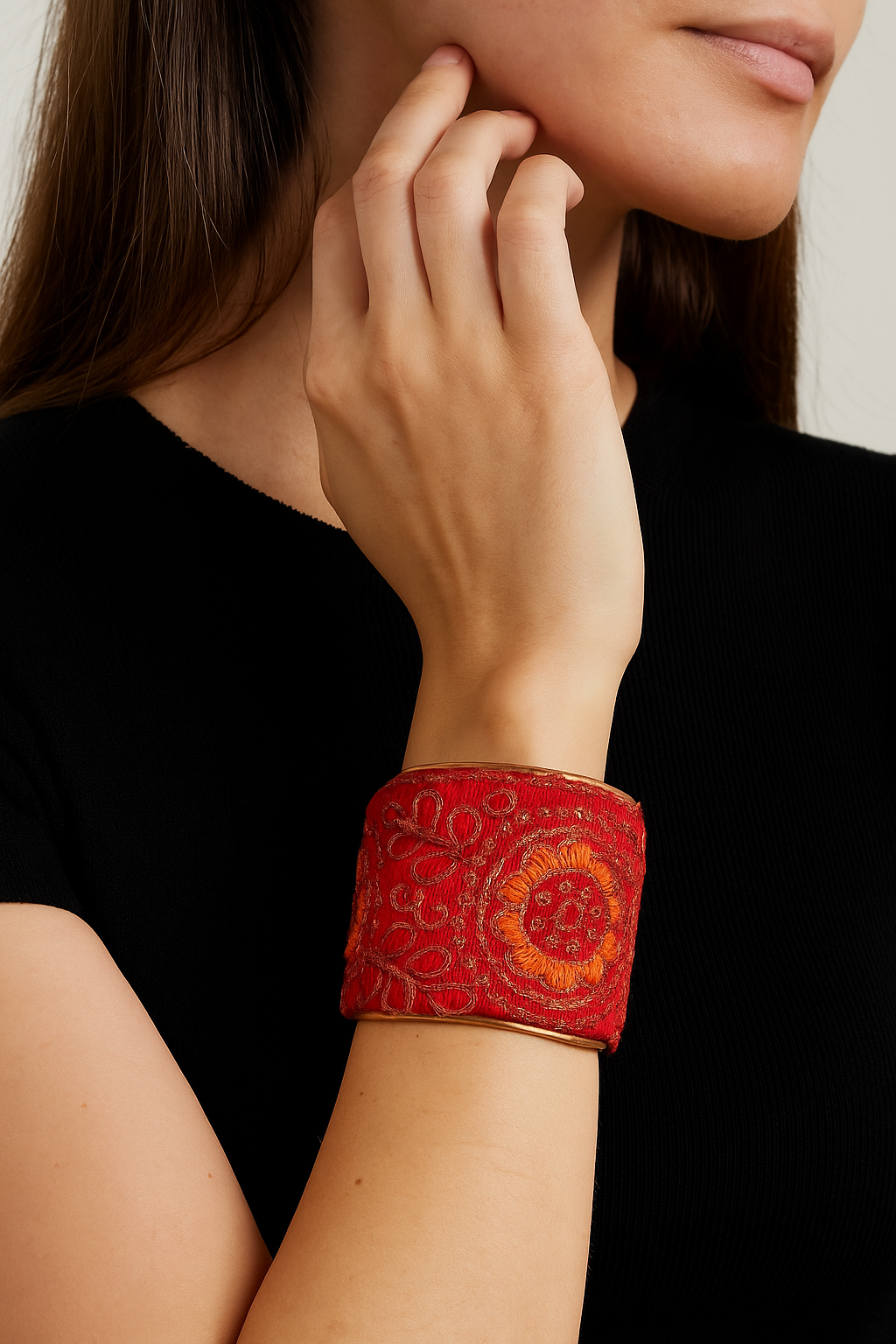 A female model wearing a one of a kind jewelry brass cuff bracelet for women—a 2-inch wide, open-back brass cuff wrapped in hand-embroidered red fabric with coral and gold floral motifs, showcased on her wrist.