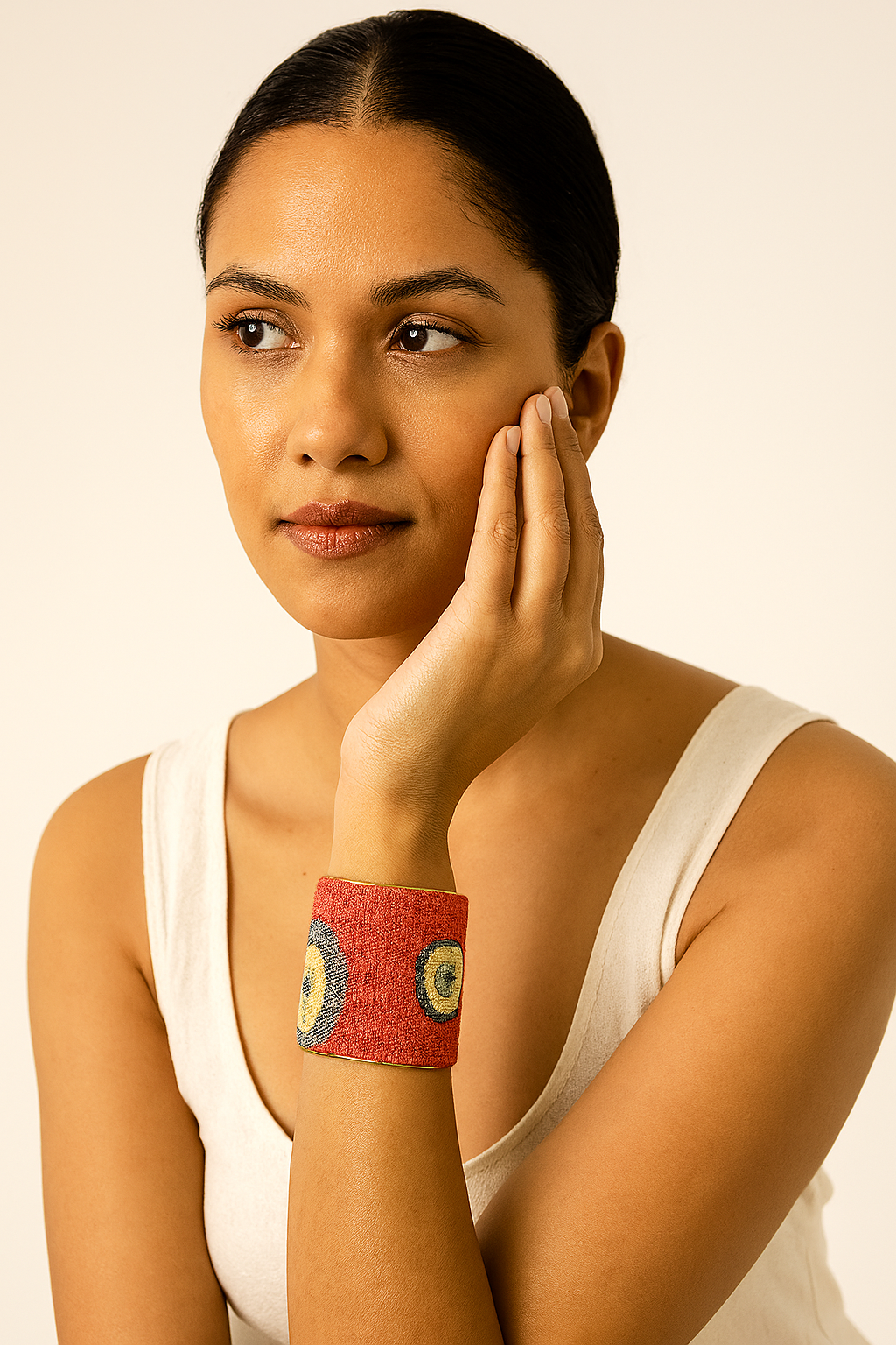 A female model wearing a one of a kind jewelry brass cuff bracelet for women—a 3-inch wide, open-back design wrapped in red tapestry fabric with teal, mustard, and navy concentric circles, showcasing its vibrant artistry on the wrist.