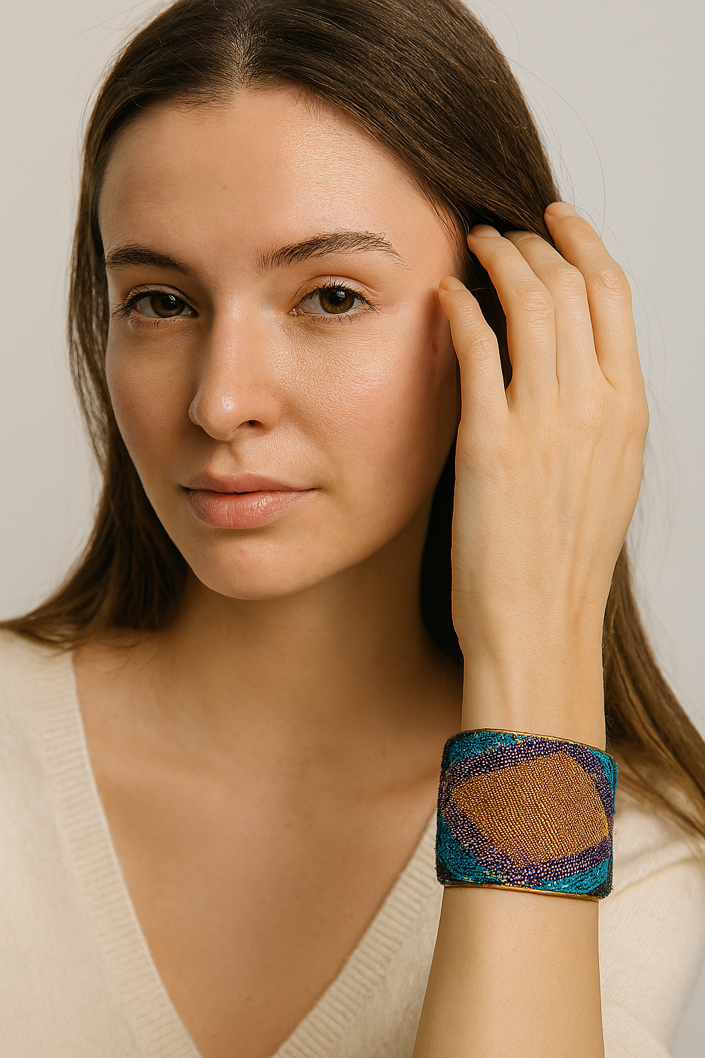 A female model wearing a one of a kind jewelry brass cuff bracelet for women—a 2-inch wide open-back design wrapped in jewel-toned woven fabric with teal, purple, and gold diamond motifs, shown on her wrist.
