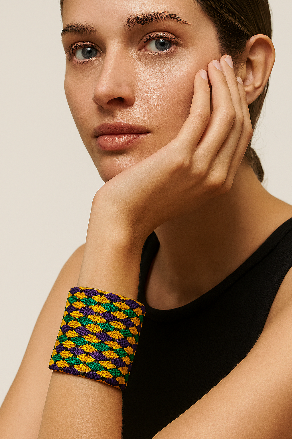 A female model wearing a one of a kind jewelry brass cuff bracelet for women—a 3-inch wide, open-back design wrapped in purple, green, and gold harlequin diamond weave with black dot accents, showcased on her wrist against a neutral background.