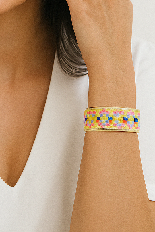 A woman wearing a 1-inch brass cuff bracelet with a vivid neon geometric woven pattern in pink, yellow, blue, and orange—styled as a fun and uplifting piece of inspirational jewelry and bold geometric bracelet.