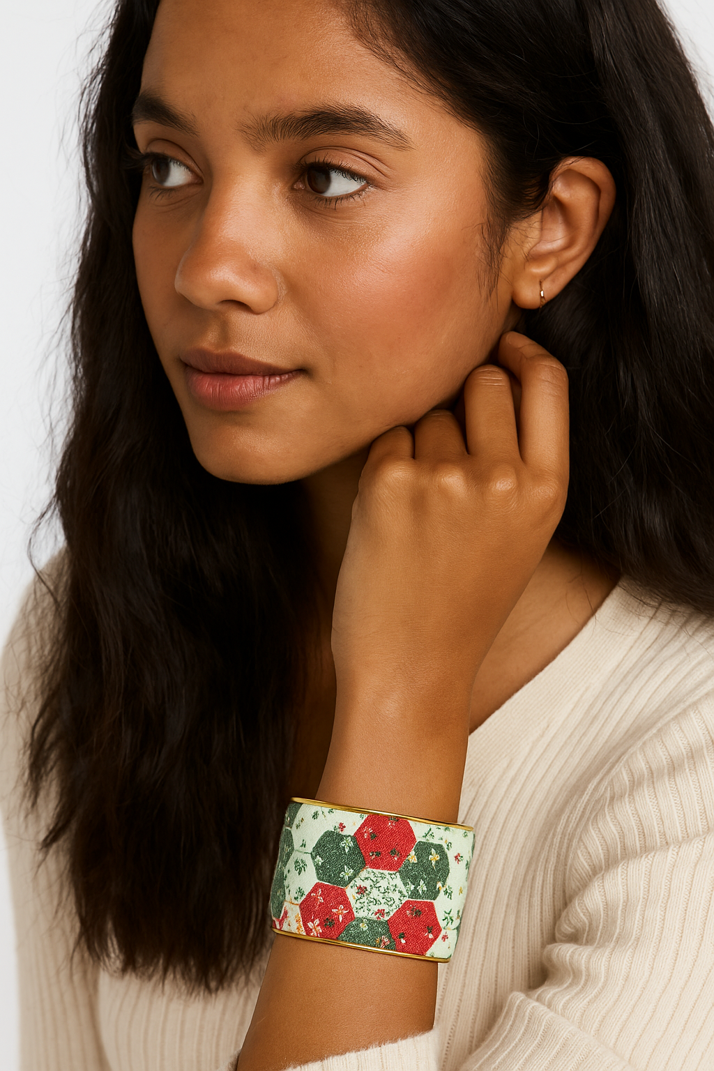 A woman wearing a 2-inch brass cuff bracelet wrapped in red and green floral cotton fabric designed to resemble vintage quilt patches. The hexagon pattern stands out against her cream sweater.