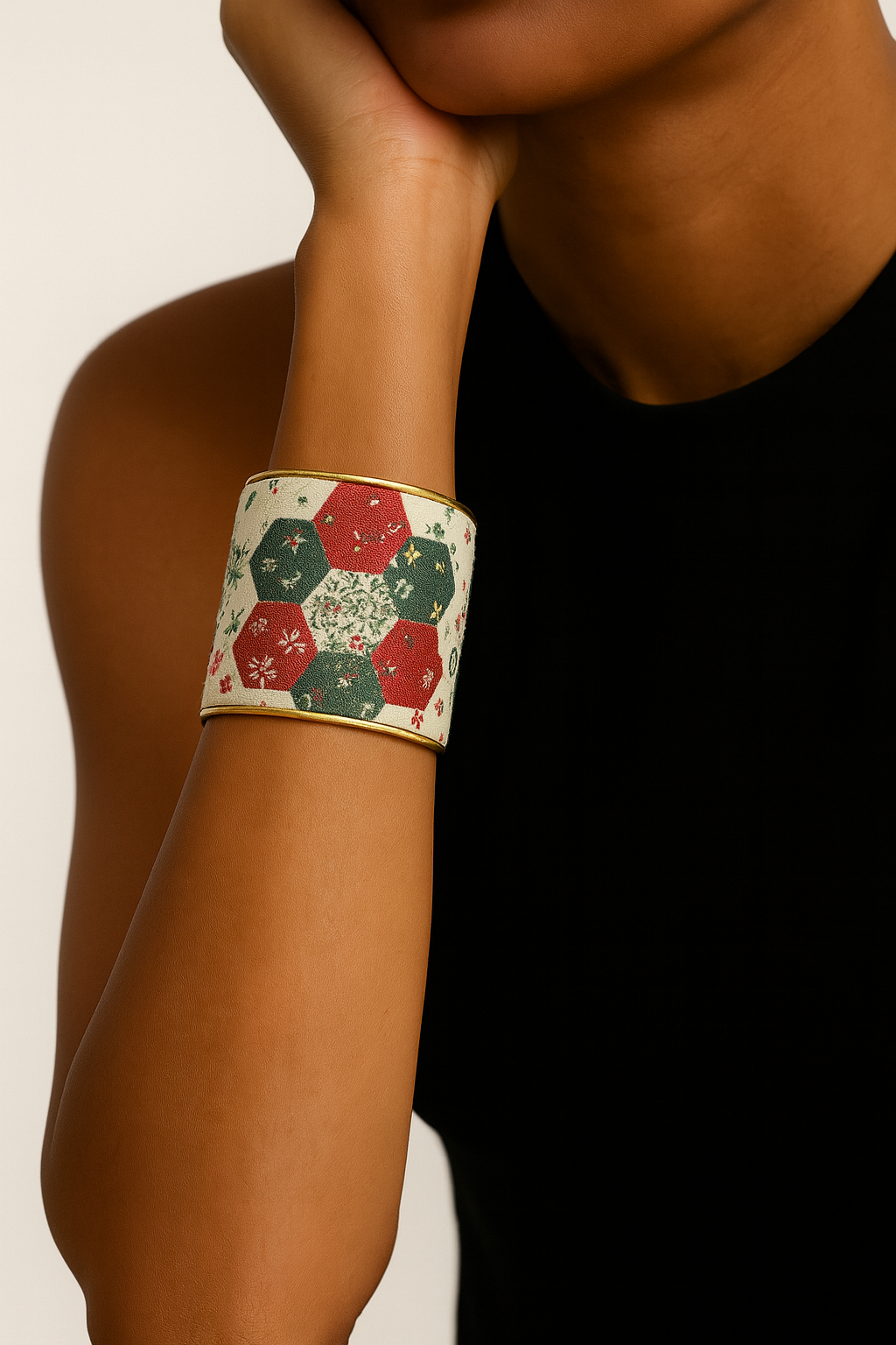 A woman wearing a 2-inch brass cuff bracelet wrapped in red and green floral cotton fabric designed to resemble vintage quilt patches. The hexagon pattern stands out against her cream sweater.