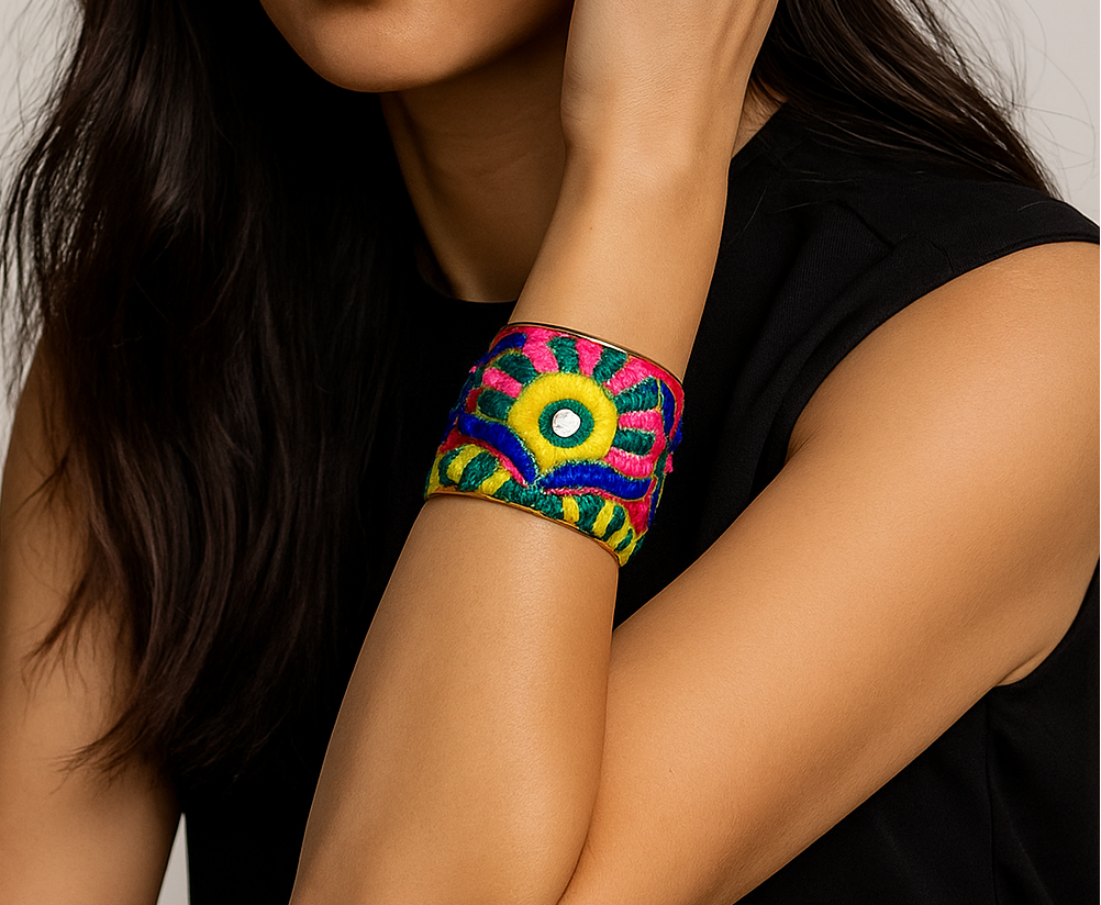 Close-up portrait of a female model wearing a 2-inch wide scarlet hand-embroidered brass cuff bracelet; the open-back ends peek out as she gently touches her hair.