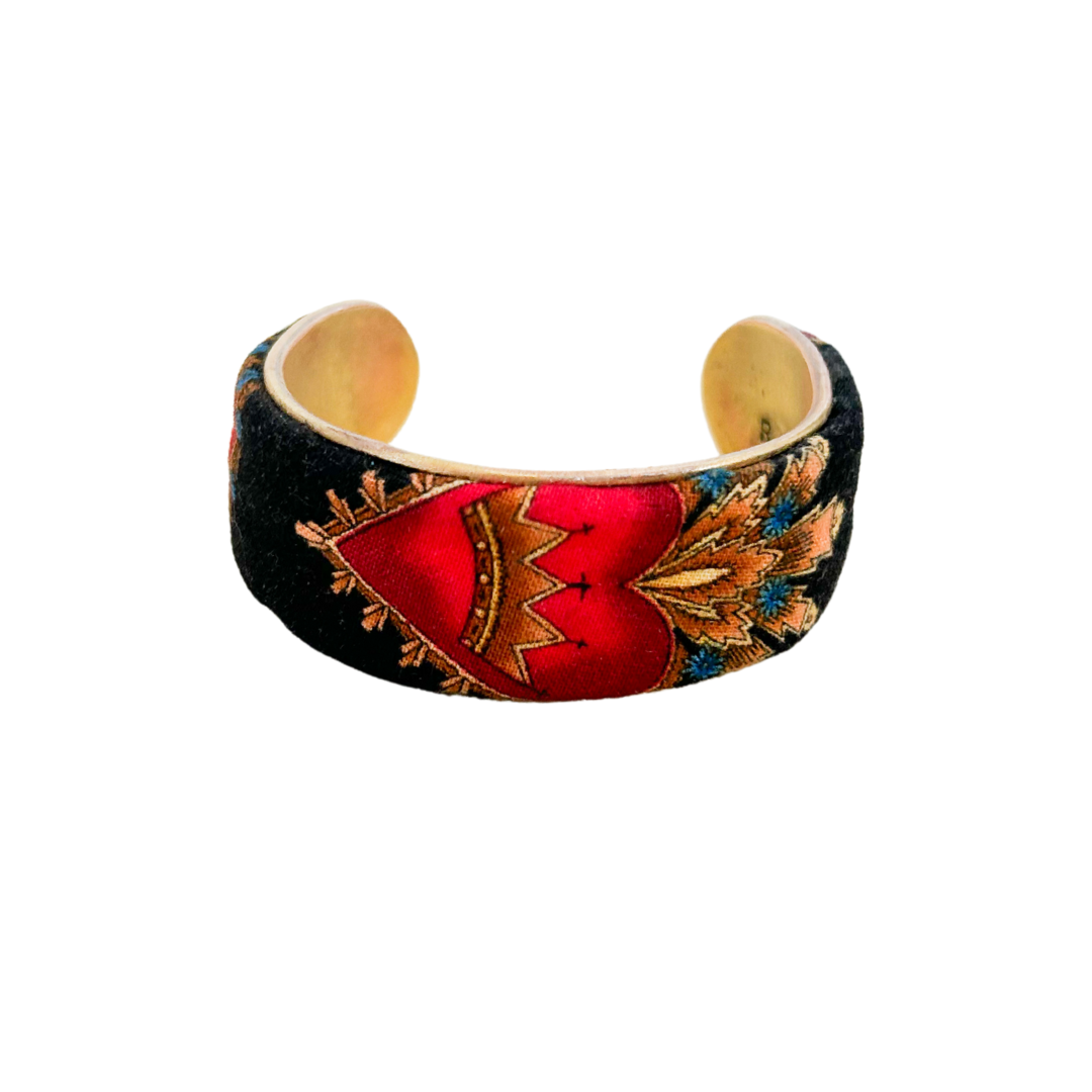 A brass cuff bracelet by Redd Dott Jewelry, featuring a black base design with a striking red sacred heart crowned in gold. This gold cuff bracelet showcases intricate beauty and flame-like detailing, creating a vintage-inspired statement piece.