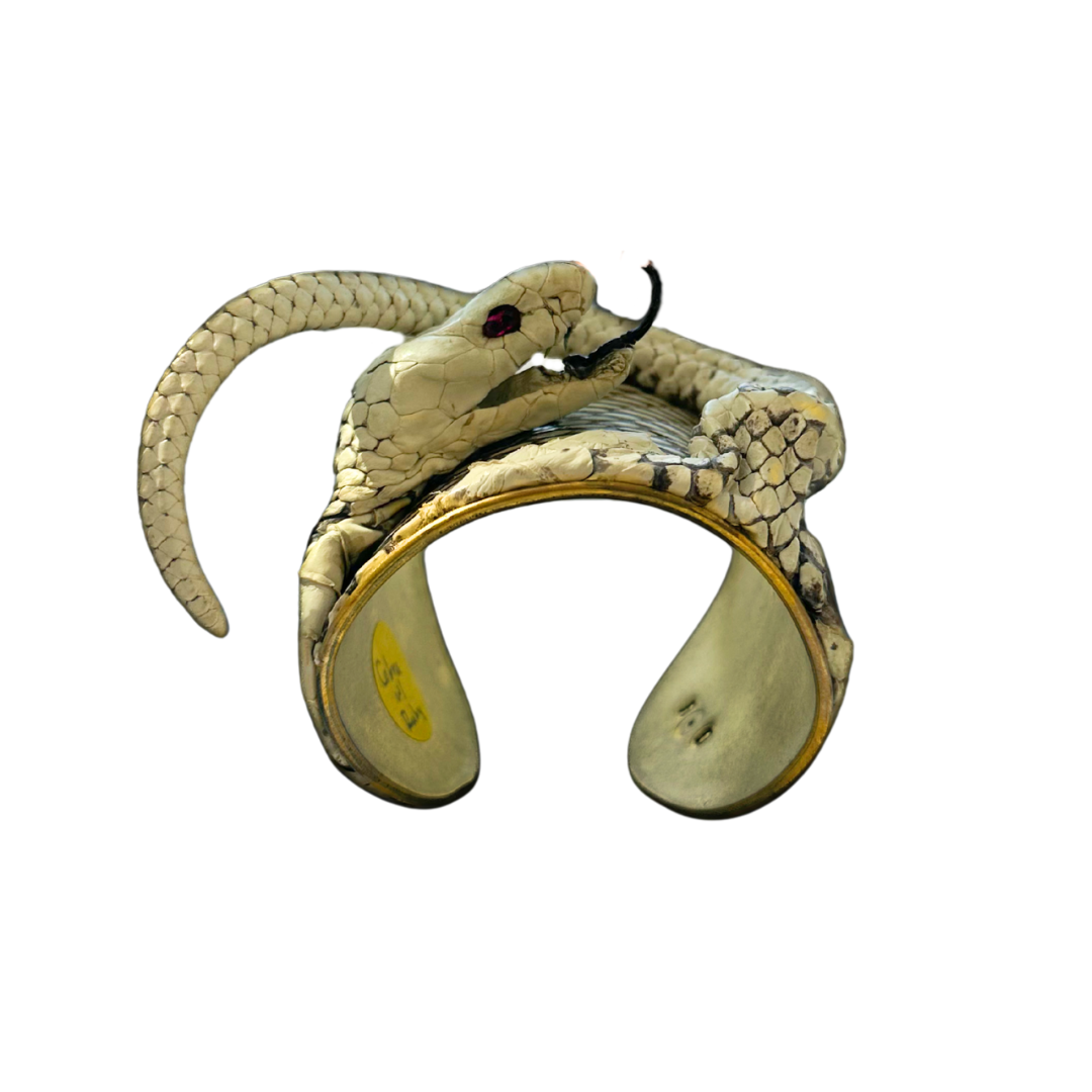 Side view of gold cuff bracelet featuring detailed cobra head and curling tail with natural snake scales and ruby eyes; one of a kind jewelry from Redd Dott × The Wild Ones.