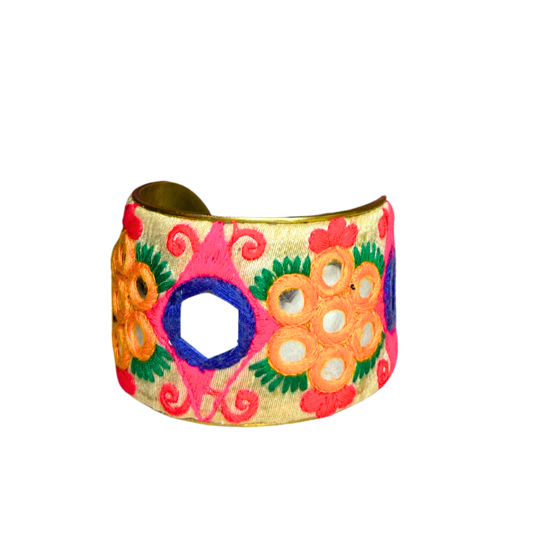 A handcrafted brass cuff bracelet by Redd Dott Jewelry with vivid pink and orange embroidery, green accents, and mirror insets. A colorful and bold engraved cuff bracelet look created with stitched detail.