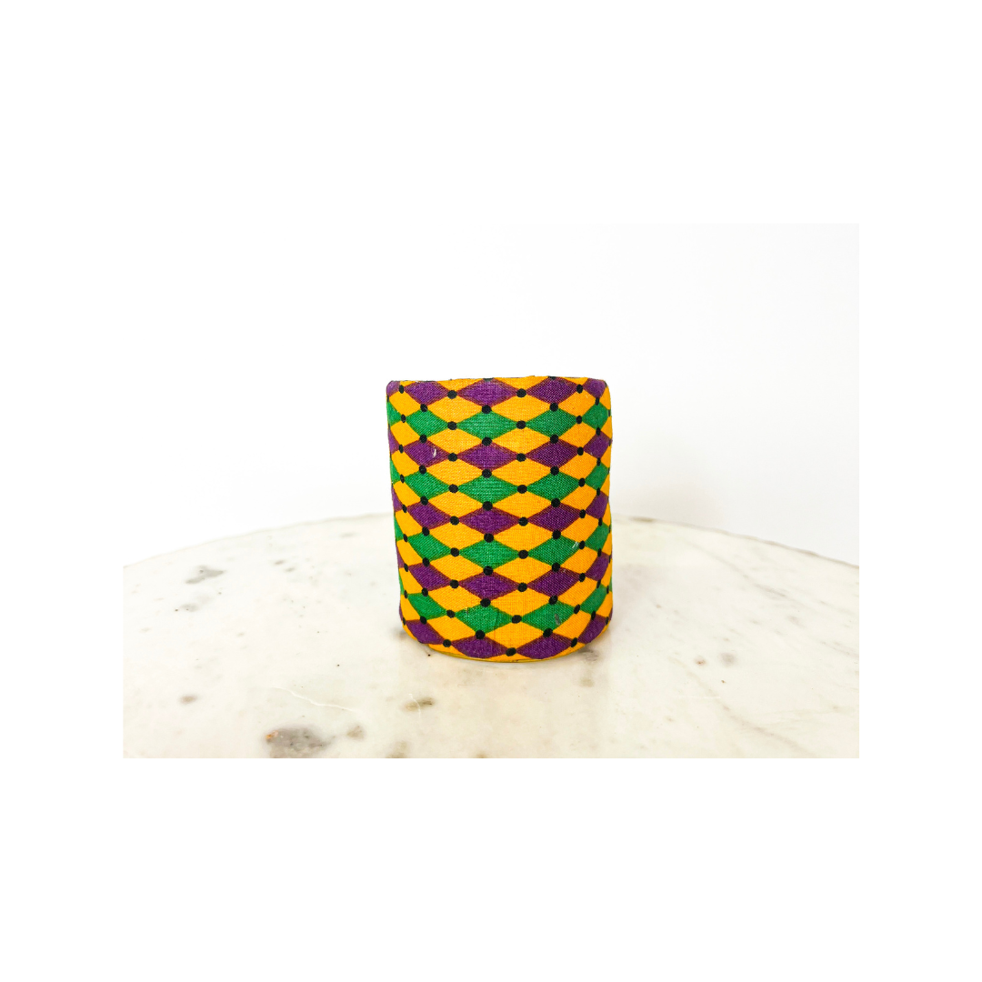 A studio image of a one of a kind jewelry brass cuff bracelet for women—available in 1-inch, 2-inch, and 3-inch widths—wrapped in purple, green, and gold jacquard diamond fabric with black dot accents, displayed on a white marble surface.
