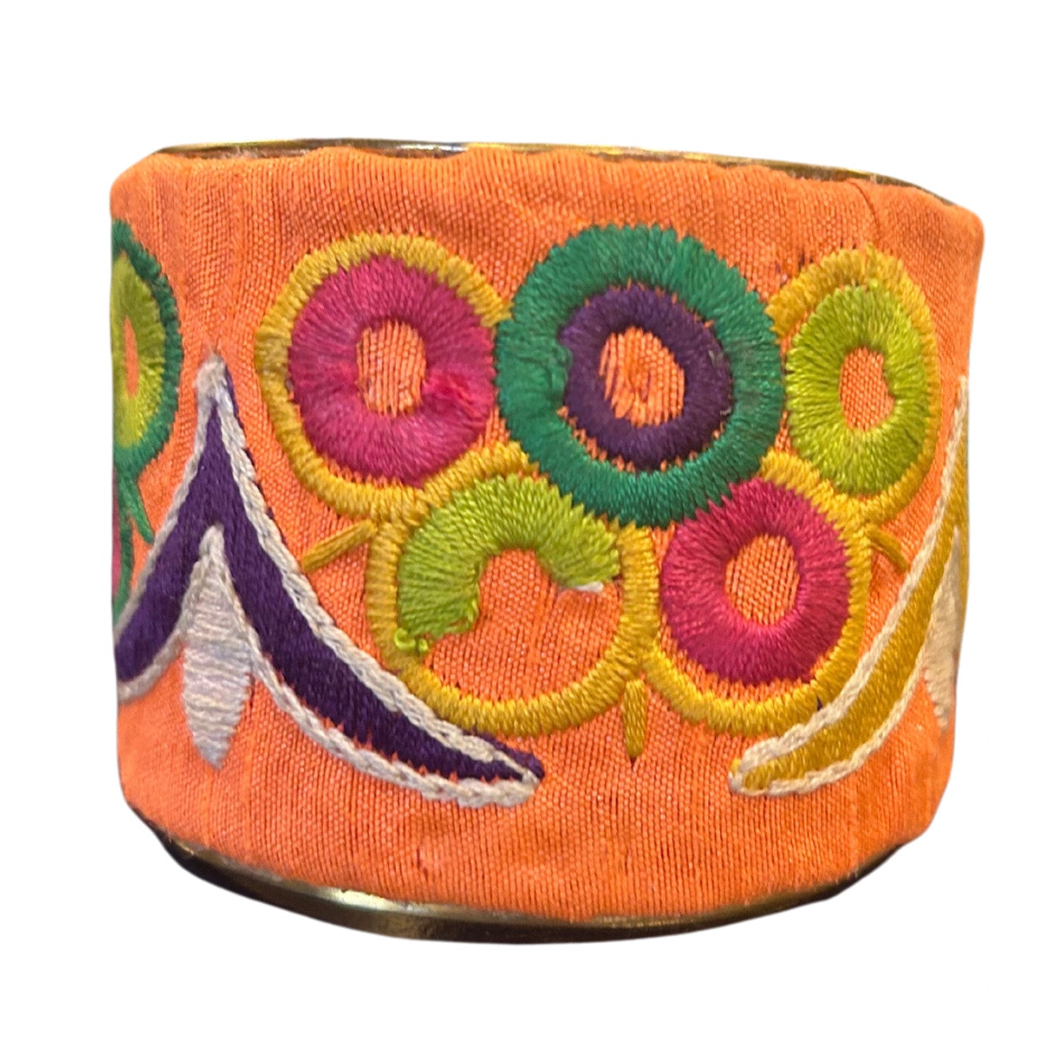 Angled view of a 2-inch wide coral velvet-wrapped brass cuff bracelet showcasing colorful embroidered floral rings in green, pink, yellow, and purple threads and the raw brass interior on a white surface.