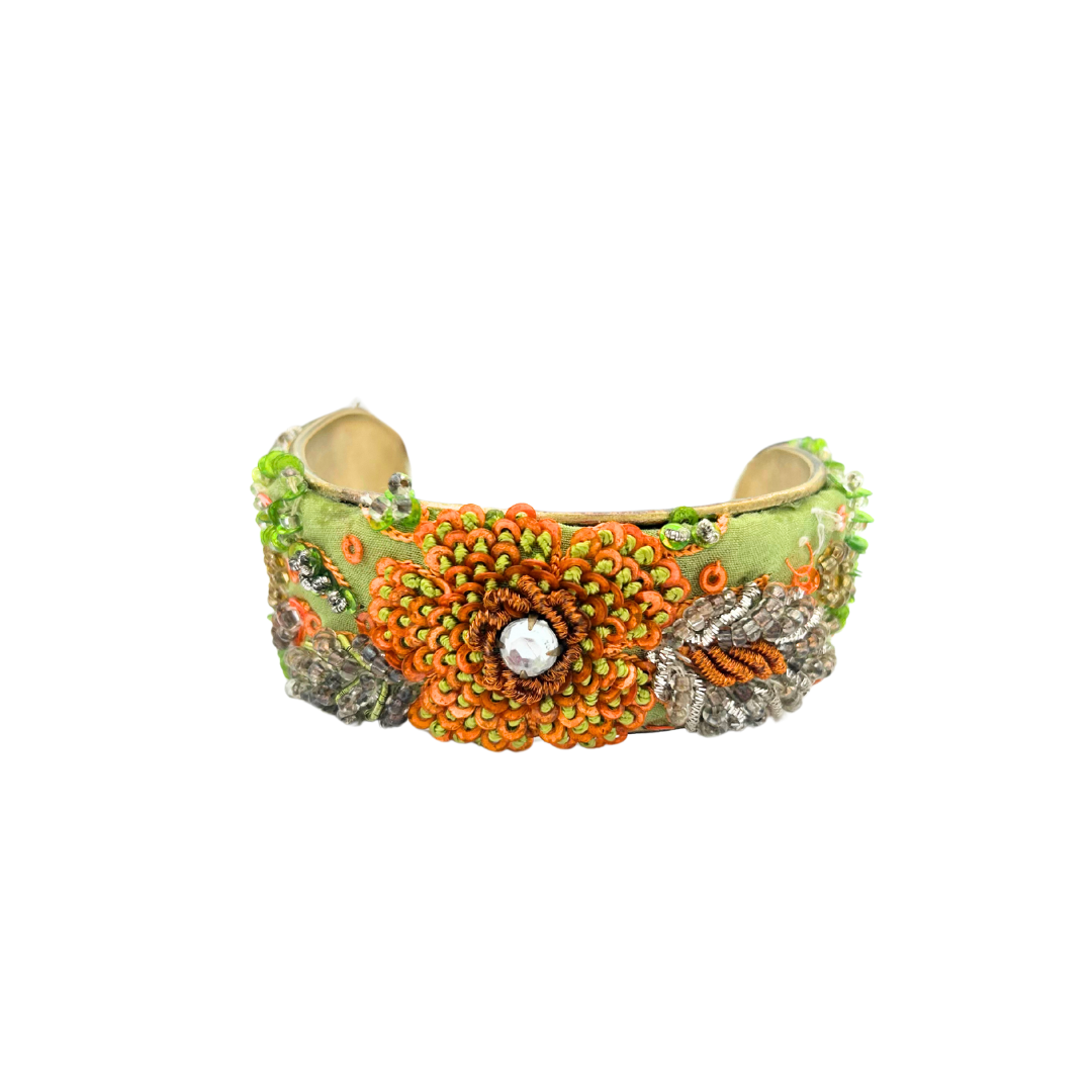 A handcrafted brass cuff bracelet by Redd Dott Jewelry featuring vibrant orange and green floral beadwork, a rhinestone centerpiece, and silver embroidered leaves on a satin green base. A bold and colorful beaded flower bracelet.