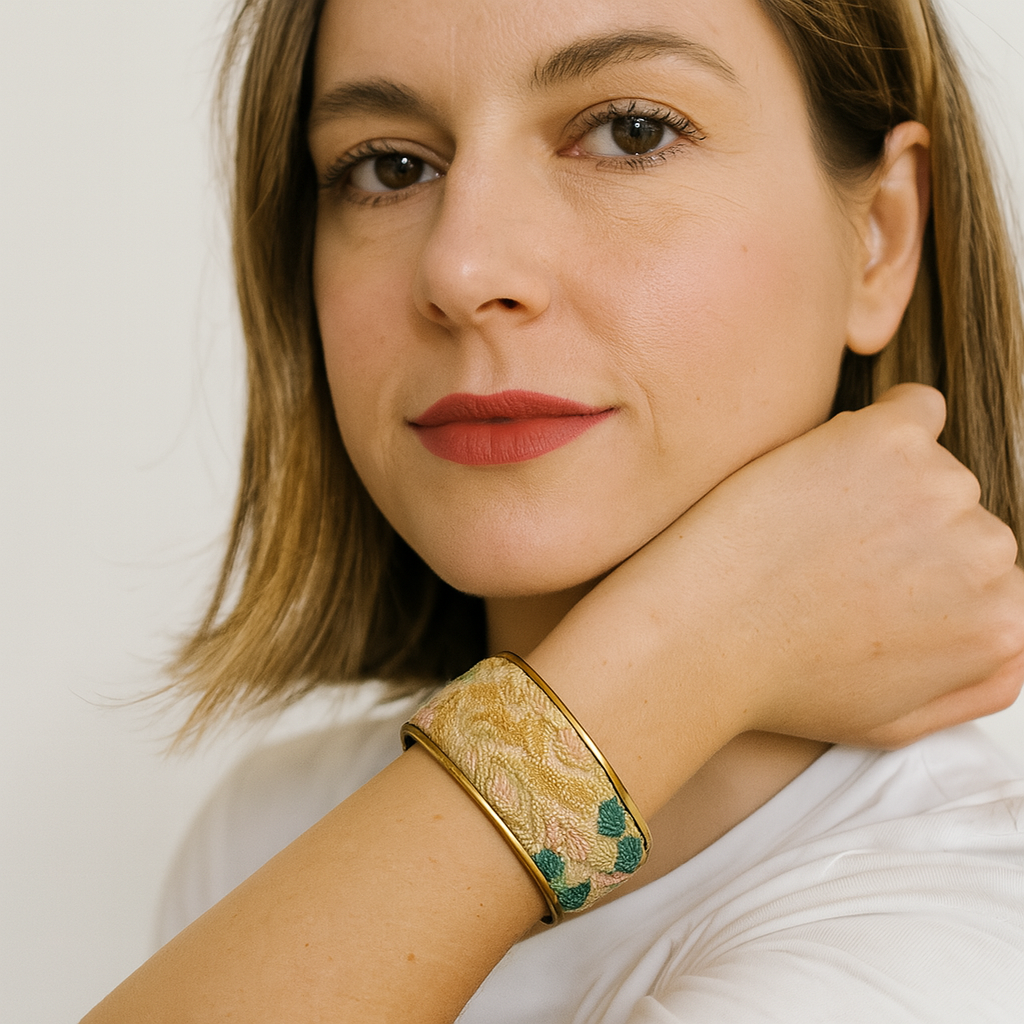 A woman wears a 1-inch brass cuff bracelet from Redd Dott Jewelry featuring a golden woven botanical fabric with hints of green and blush, embodying nature inspired jewelry and inspirational jewelry.