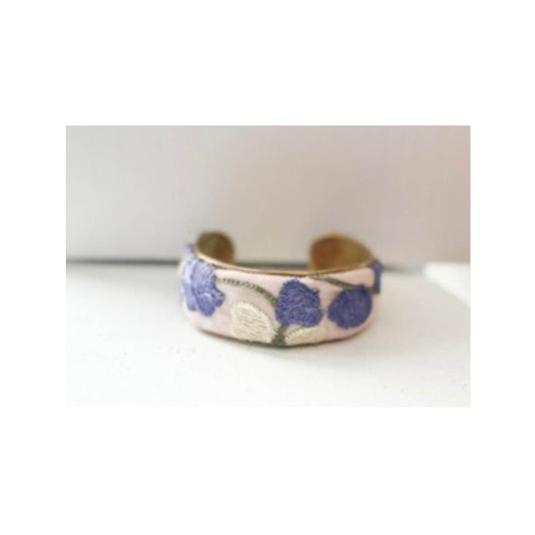 A vintage brass cuff with a floral design in purple and white on a light background displayed on a white surface.