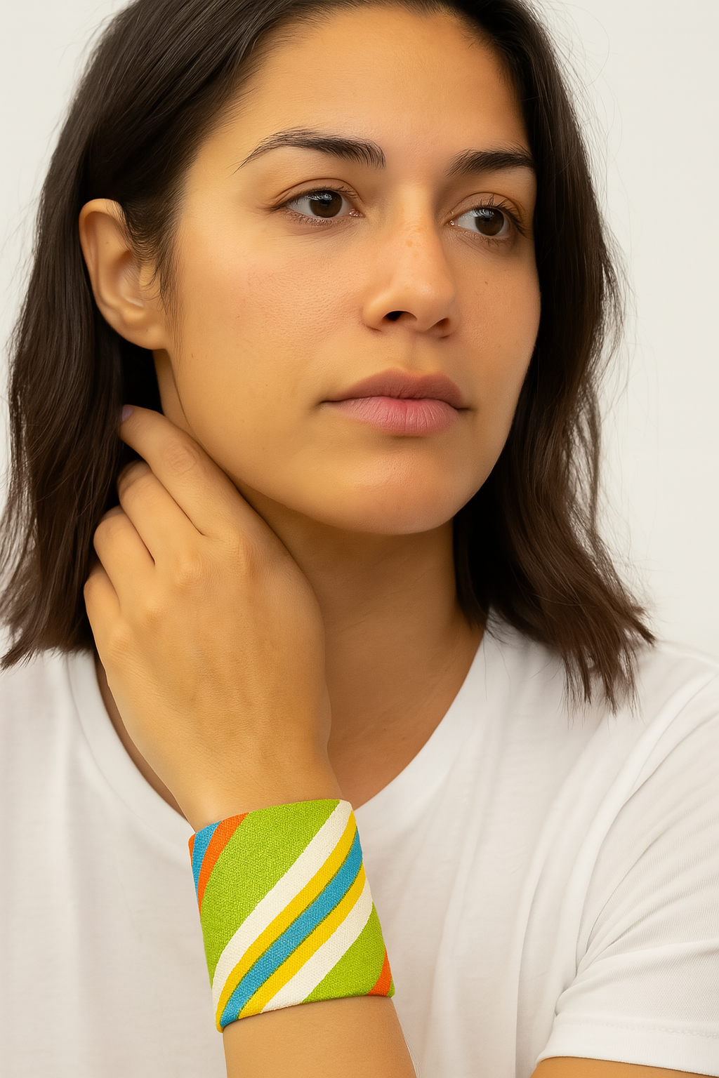 A female model resting her hand near her face while wearing a 2-inch wide raw brass cuff bracelet wrapped in lime-green linen and hand-stitched with diagonal turquoise, yellow, orange, and white stripes. This brass cuff bracelet is a unique, one of a kind jewelry piece and perfect among cuff bracelets for women.