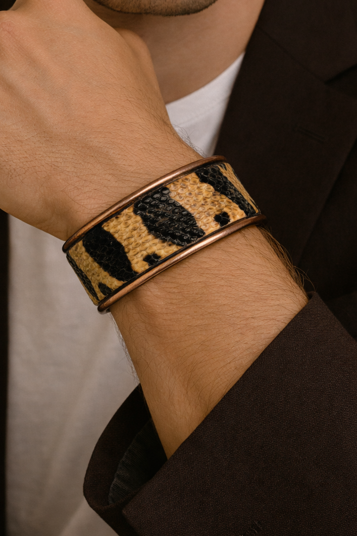 Close-up of a model wearing the men’s 1-Inch bull snake skin cuff bracelet by Redd Dott Jewelry, featuring bold black and golden tan snake skin pattern with natural scale texture set into a slim brass cuff, highlighting the striking contrast and handcrafted cuff bracelet detail, handcrafted in Shreveport, LA by Redd Dott Jewelry.