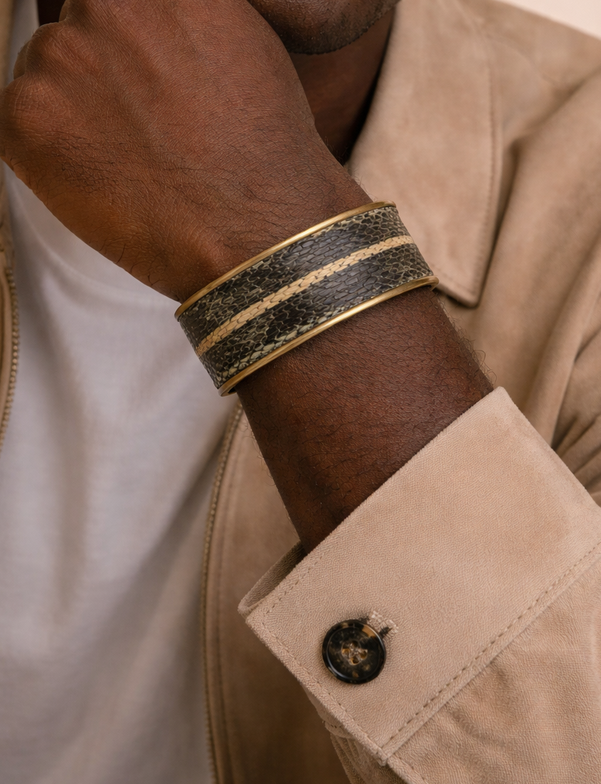 Close-up of a model wearing the men’s 1-inch garter snake skin cuff bracelet by Redd Dott Jewelry, featuring dark olive and charcoal snake pattern with a pale natural stripe running through the center, framed in a slim brass cuff that highlights the organic scale texture and handcrafted detail, handcrafted in Shreveport, LA by Redd Dott Jewelry.