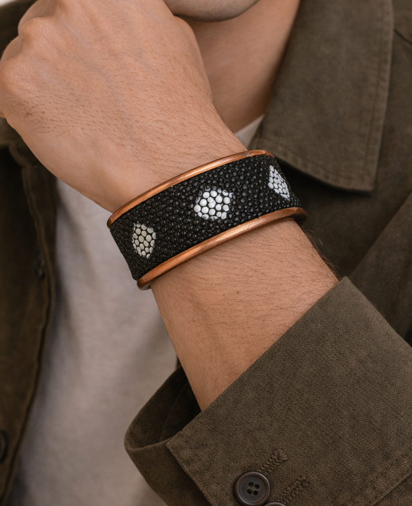 Close-up of a model wearing the men’s 1-inch stingray skin cuff bracelet by Redd Dott Jewelry, featuring deep black stingray leather with natural white diamond-shaped bead pattern, framed by warm copper-toned brass edges that highlight the tactile texture and bold handcrafted cuff bracelet design, handcrafted in Shreveport, LA by Redd Dott Jewelry.