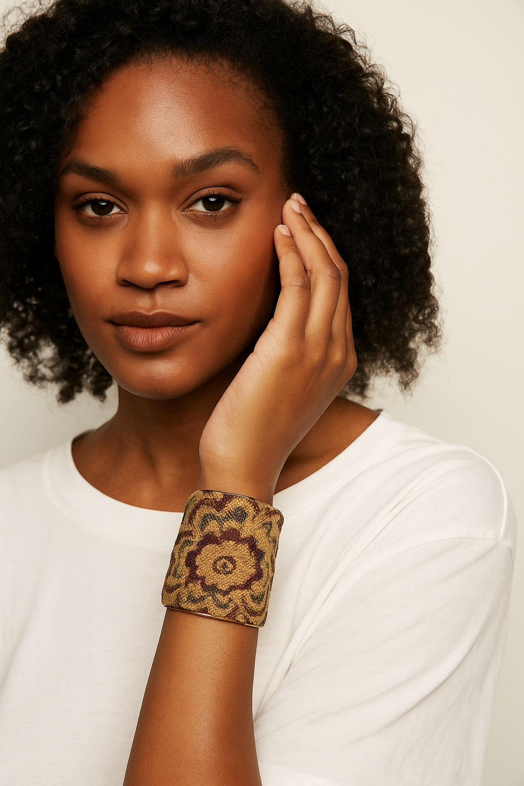 A three-inch brass cuff bracelet wrapped in gold, burgundy, and navy tapestry fabric with a floral medallion design, shown on a female model 