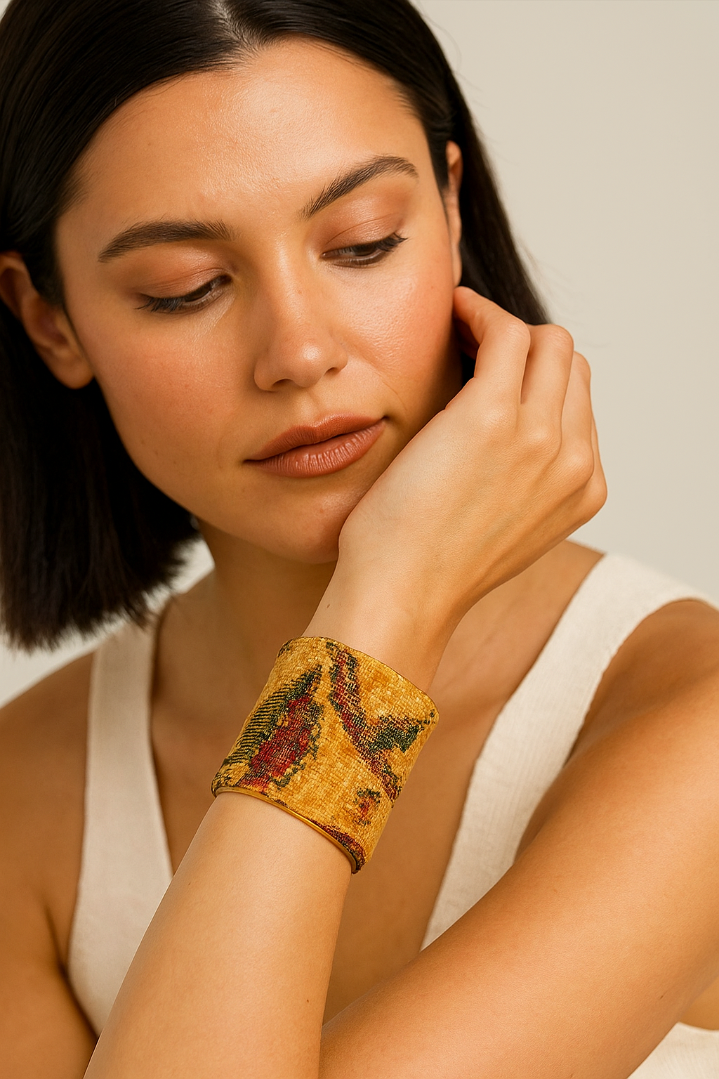 A female model wearing a three-inch brass cuff bracelet wrapped in yellow tapestry fabric embroidered with green and red paisley swirls