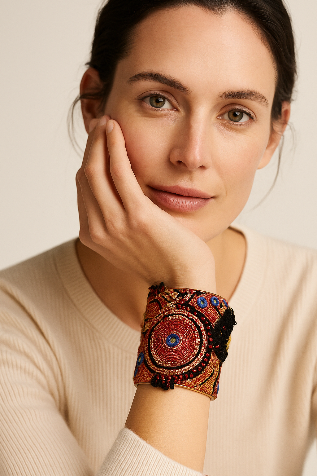 A 3-inch brass cuff bracelet wrapped in embroidered fabric with red and gold circles, blue highlights, and black fringe, shown on the wearer’s wrist against a neutral background.