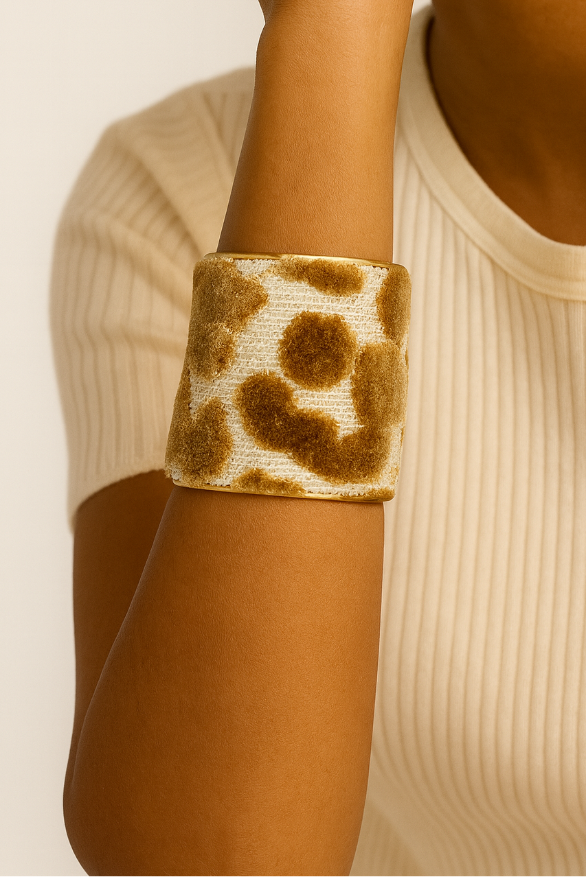 Close-up of a model wearing the Kylen 3-Inch cuff bracelet, featuring a soft ivory textile with warm tan abstract spots wrapped around a wide brass cuff, highlighting the bold scale and tactile surface of this handcrafted jewelry piece, handcrafted in Shreveport, LA by Redd Dott Jewelry.