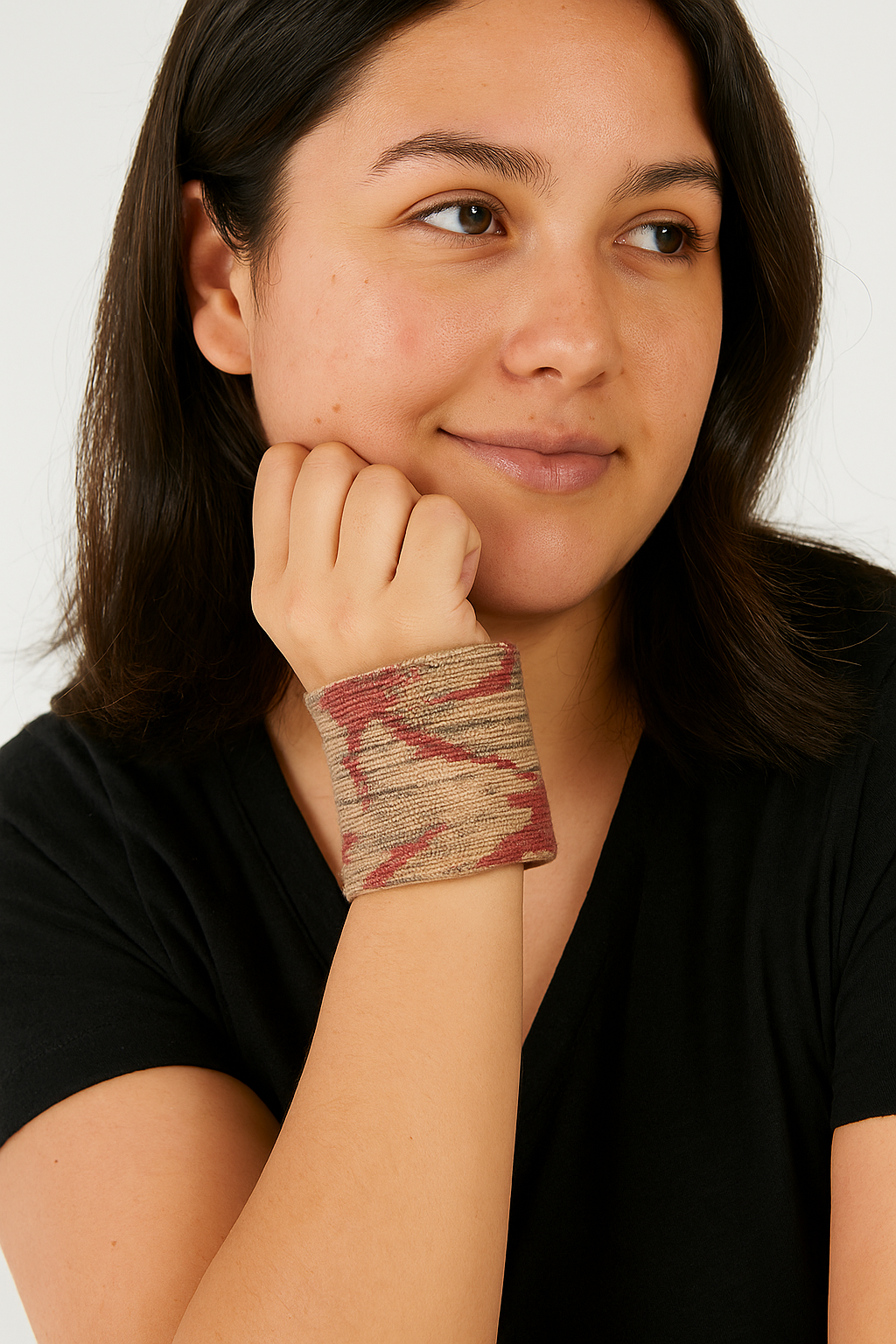 Female model with dark hair wearing a black top, resting her chin on her hand and showcasing a 3-inch wide brass cuff bracelet wrapped in neutral beige fabric with red abstract accents on her left wrist. A modern statement among cuff bracelets for women.