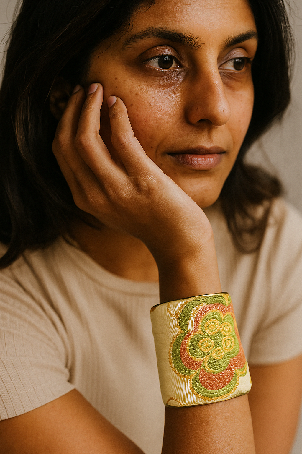 A female model’s wrist adorned with a 3-inch raw brass cuff bracelet featuring ivory fabric embroidered in coral and green floral patterns—an eye-catching one of a kind jewelry statement among cuff bracelets for women.