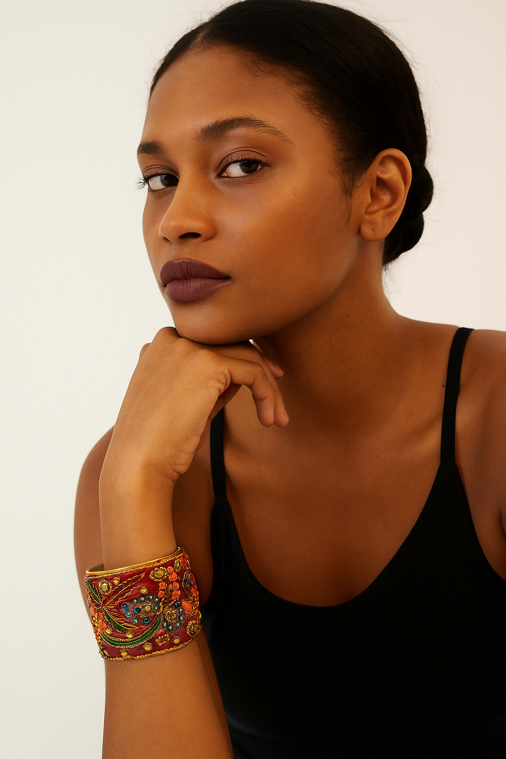 Female model with braided hair wearing a black tank top, showing a 2-inch wide brass cuff bracelet wrapped in red silk sari fabric with gold embroidery and multicolored beadwork on her left wrist. A bold example of one of a kind jewelry and standout cuff bracelets for women.