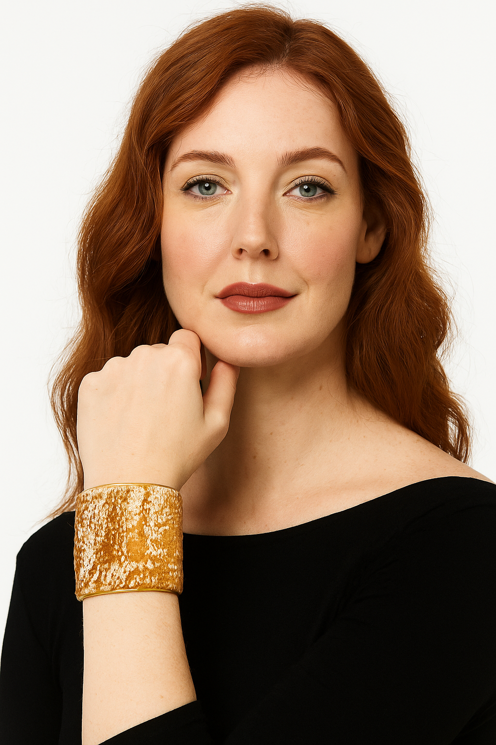 Female model with red hair wearing a black top, resting her chin on her hand and showcasing a 3-inch wide brass cuff bracelet wrapped in amber and ivory textured velvet on her left wrist. A striking example of cuff bracelets for women.