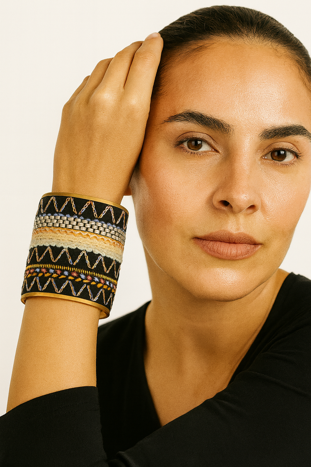 Close-up of a woman wearing the Redd Dott Eloise 3-inch gold cuff bracelet, featuring a black fabric base with layered embroidery in cream, orange, and multicolor geometric patterns accented by metallic details.