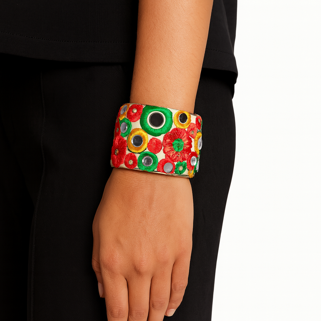 Close-up of the Redd Dott Margot 2-inch cuff bracelet, featuring bold red, green, and yellow embroidered florals accented with tiny mirrorwork details, framed in polished brass for a vibrant and artistic statement.