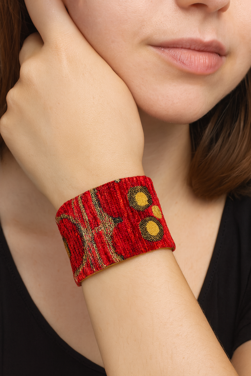 Model wearing the Redd Dott Marisol 2-inch cuff bracelet, featuring bold red fabric embroidered with golden circles and flowing abstract designs, creating a striking statement piece framed in brass.
