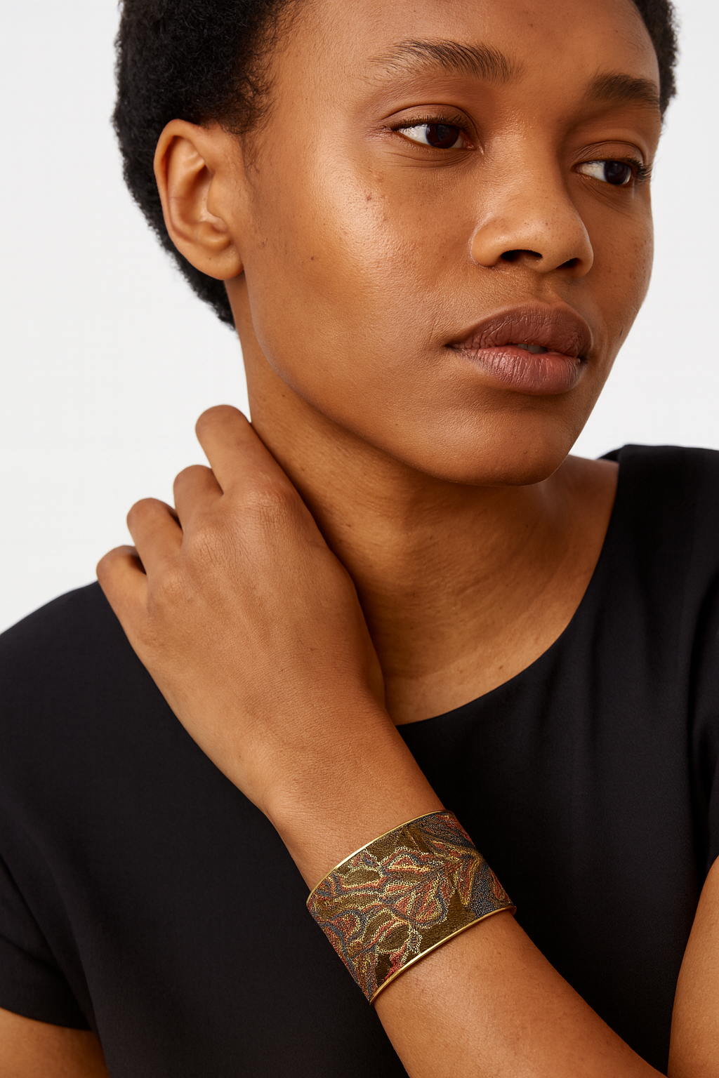 Model wearing the Redd Dott Melantha 2-inch cuff bracelet, featuring an intricate embroidered botanical pattern in earthy tones of gold, red, and green, set against a shimmering dark backdrop with a polished gold frame.