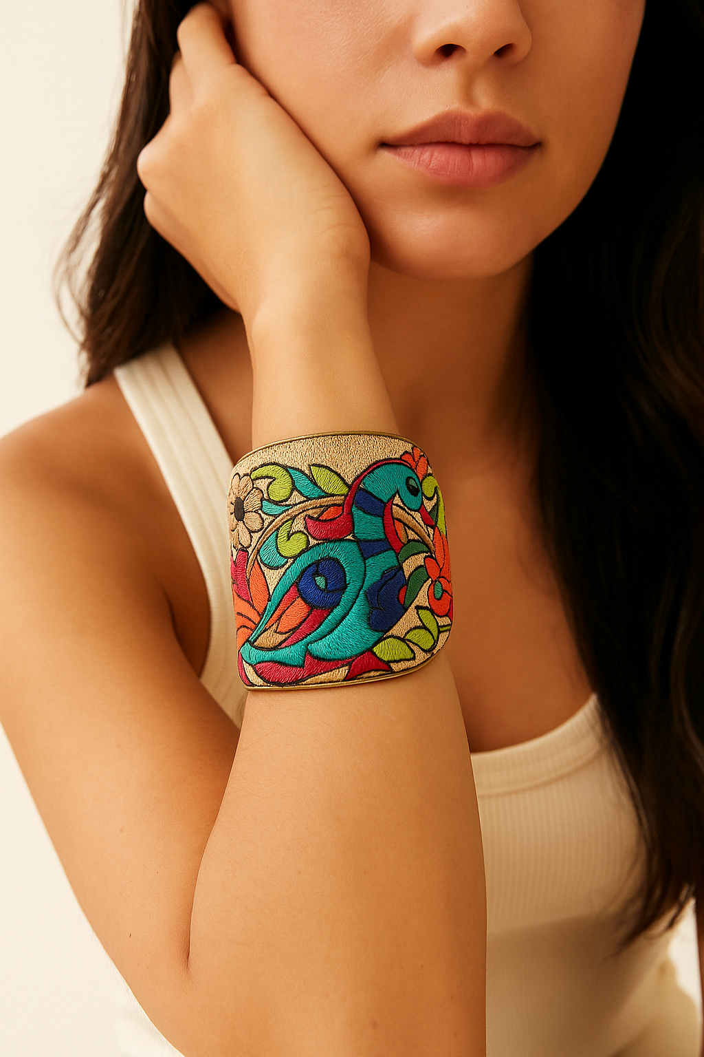 Model wearing the Redd Dott Micaela 3-inch cuff bracelet, featuring a vibrant embroidered toucan design in shades of turquoise, blue, and red, surrounded by lush green leaves and floral accents on a golden backdrop, framed in gold.