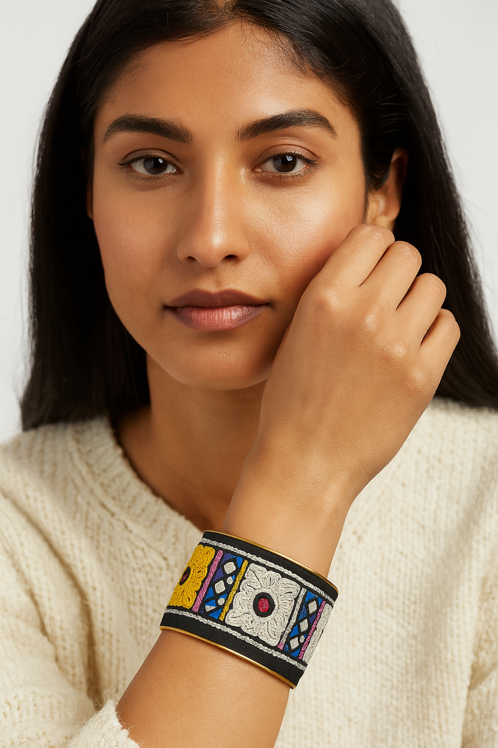 Model wearing the Redd Dott Nahla 2-inch cuff bracelet, featuring bold embroidered geometric and floral patterns in yellow, white, pink, and blue on a black base with gold edging.
