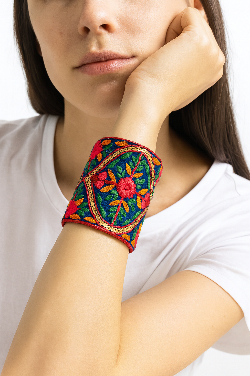 Model wearing the Redd Dott Neha 3-inch cuff bracelet, richly embroidered in bold red and orange florals with green leaves on a deep blue base, accented with gold detailing for an ornate statement look.