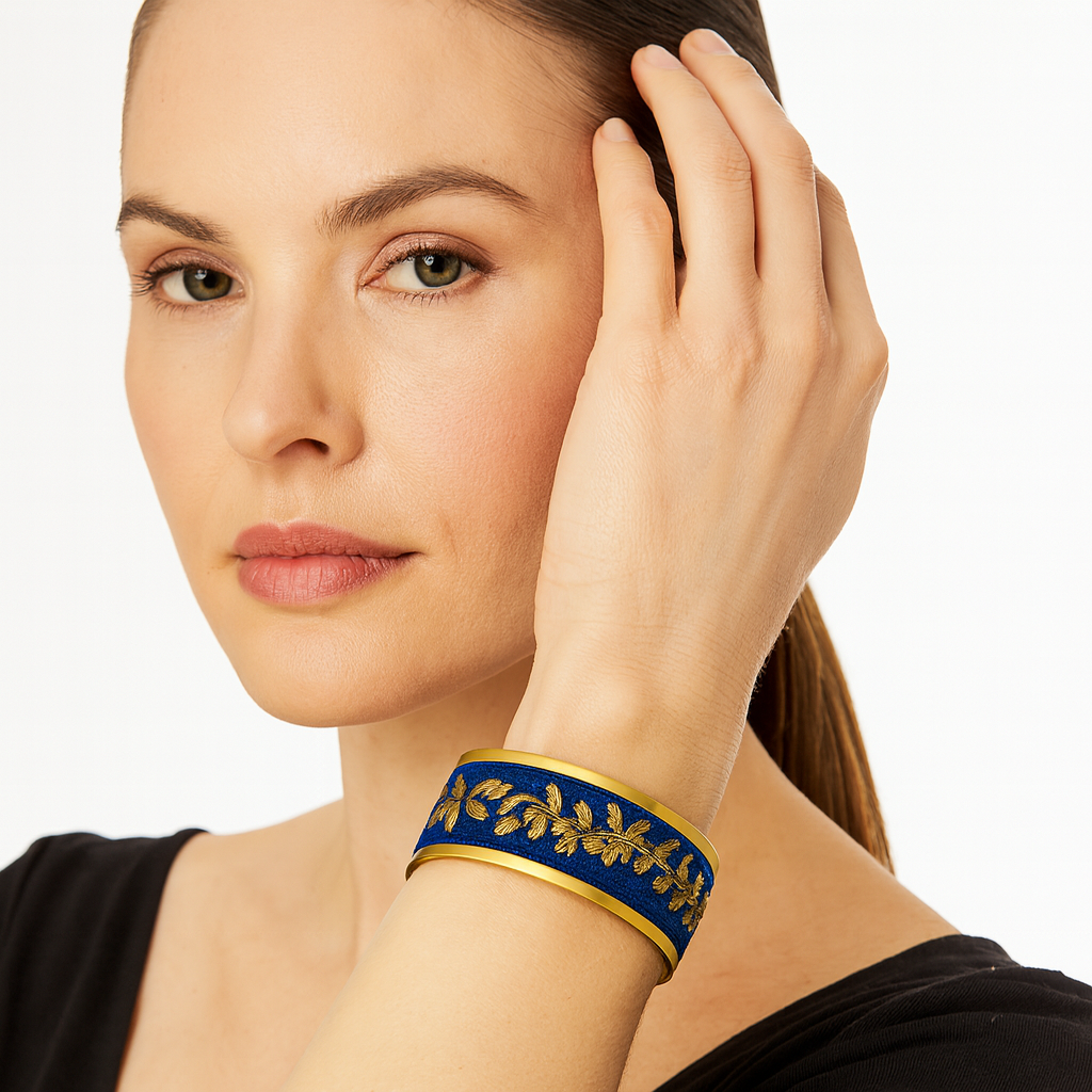 Model wearing the Redd Dott Neola 1-inch cuff bracelet, featuring a deep royal blue base with golden laurel embroidery, framed in gold-toned edging for a regal finish.