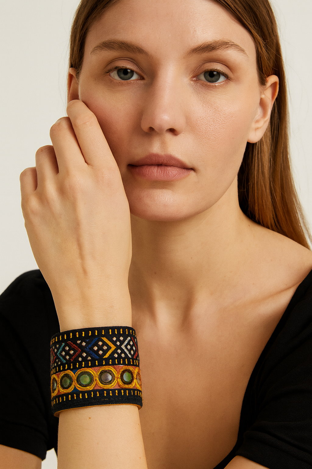 Model wearing the Redd Dott Neriyah 2-inch cuff bracelet, designed with intricate geometric embroidery in bold colors and accented with a row of circular gem-like embellishments against a deep black base.