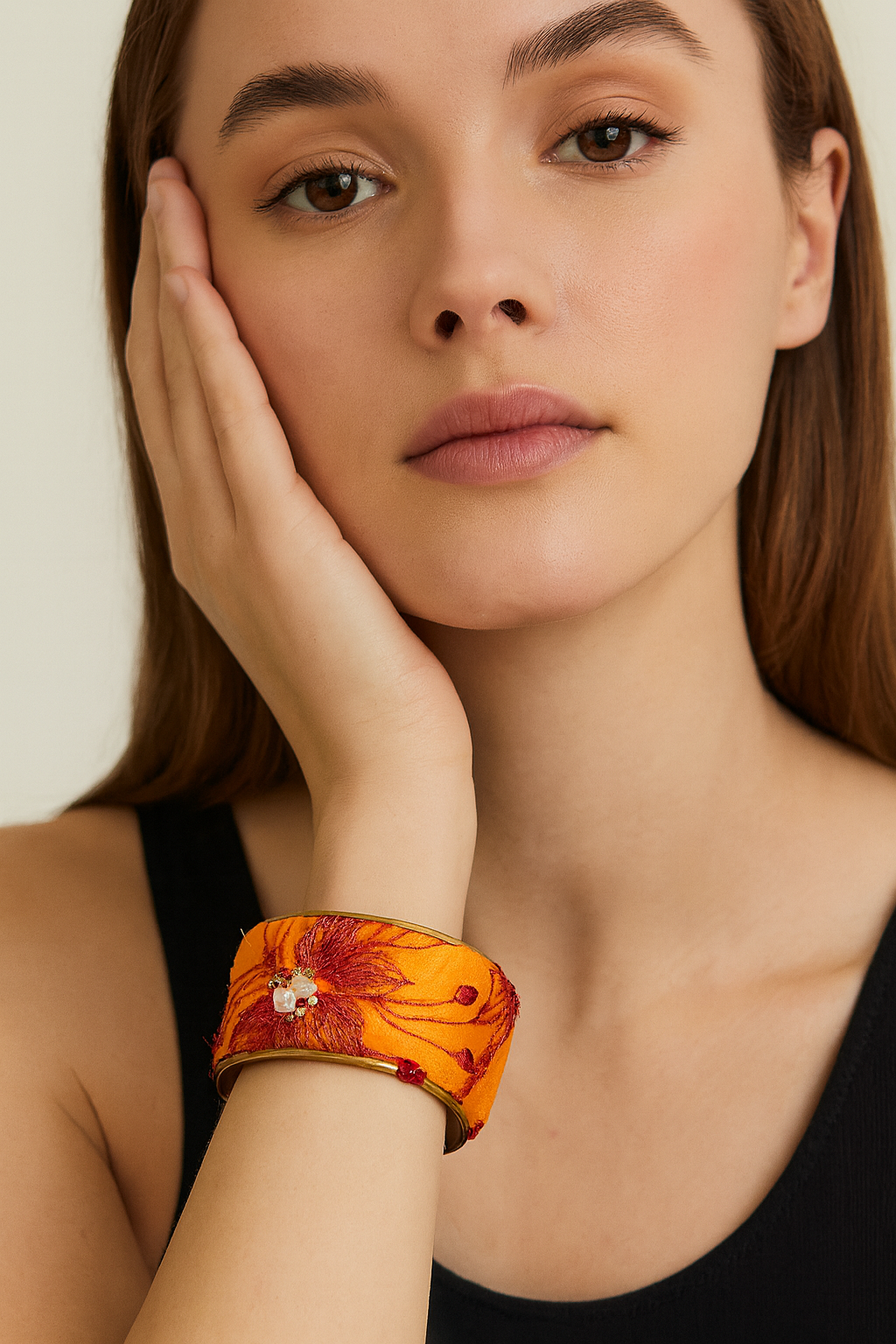 Model wearing the Redd Dott Neve 1-inch cuff bracelet, crafted in vivid golden-orange fabric with embroidered red floral detailing, accented by a delicate beaded embellishment at the center.