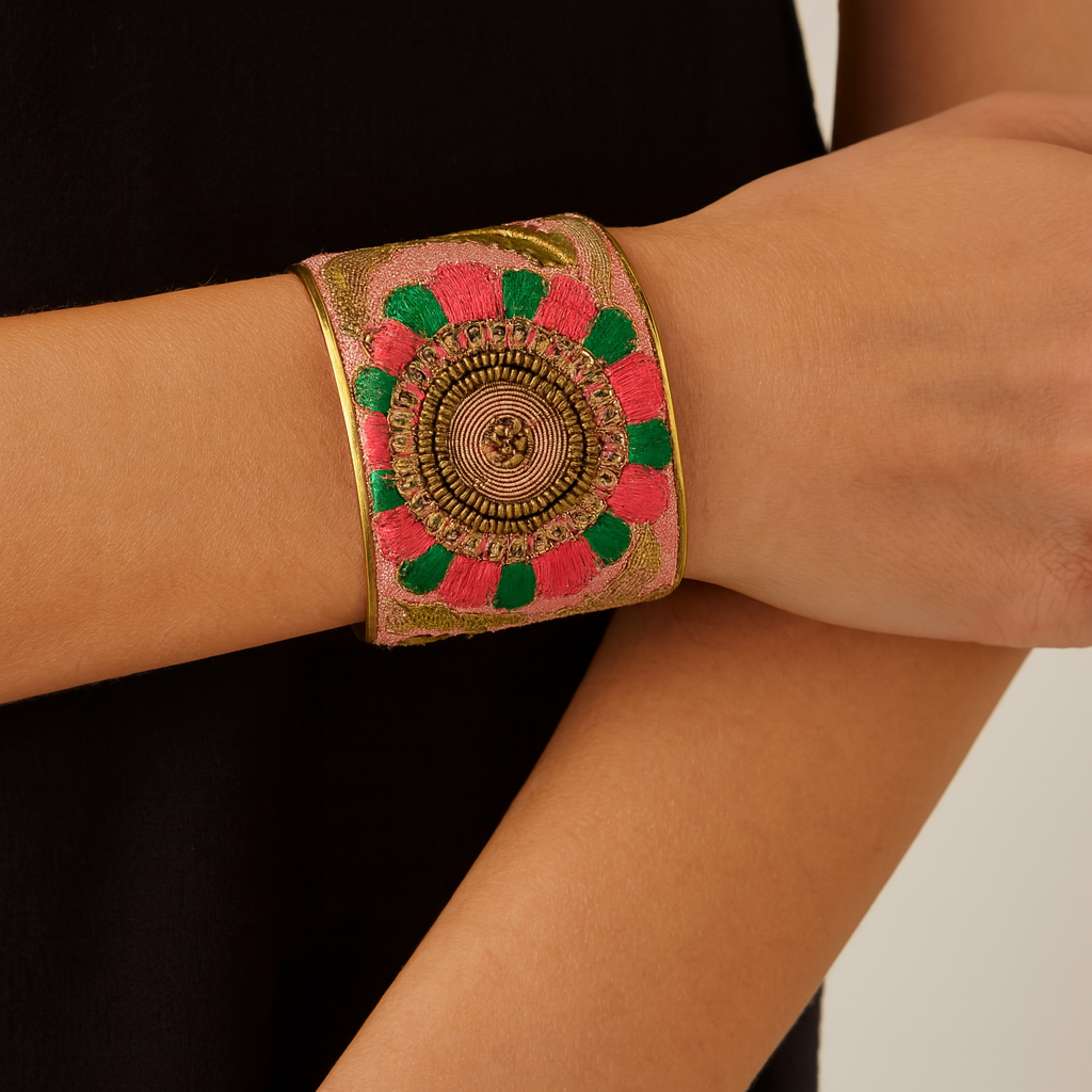 Close-up of a woman wearing the Redd Dott Ophelia 2-inch gold cuff bracelet, featuring a bold circular centerpiece with pink and green embroidered petals surrounding intricate metallic detailing.
