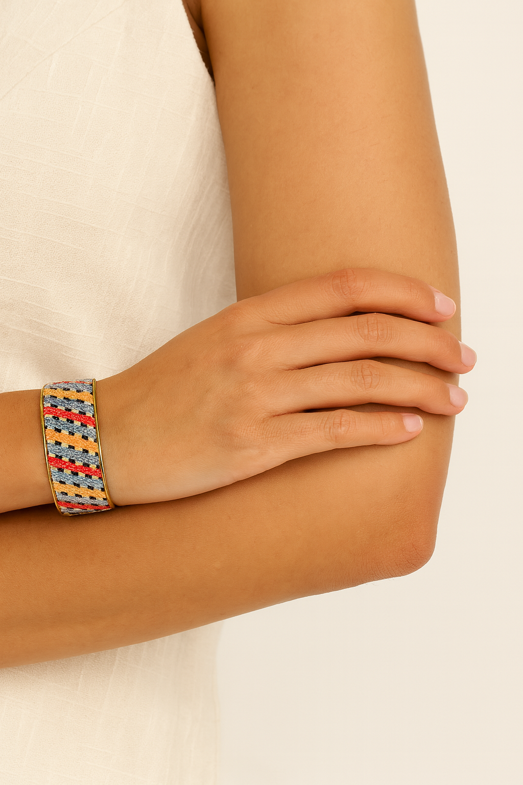 Close-up of a woman’s arm wearing the Redd Dott Phebe 1-inch cuff bracelet, featuring a woven geometric pattern in red, yellow, blue, gray, and black with a gold frame.
