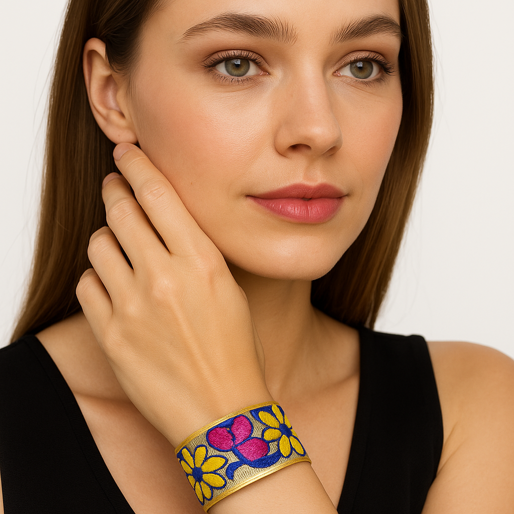 Close-up of a woman wearing the Redd Dott Philomena 1-inch cuff bracelet, featuring bold embroidery with bright yellow flowers and a magenta accent on a deep blue background, framed in gold.