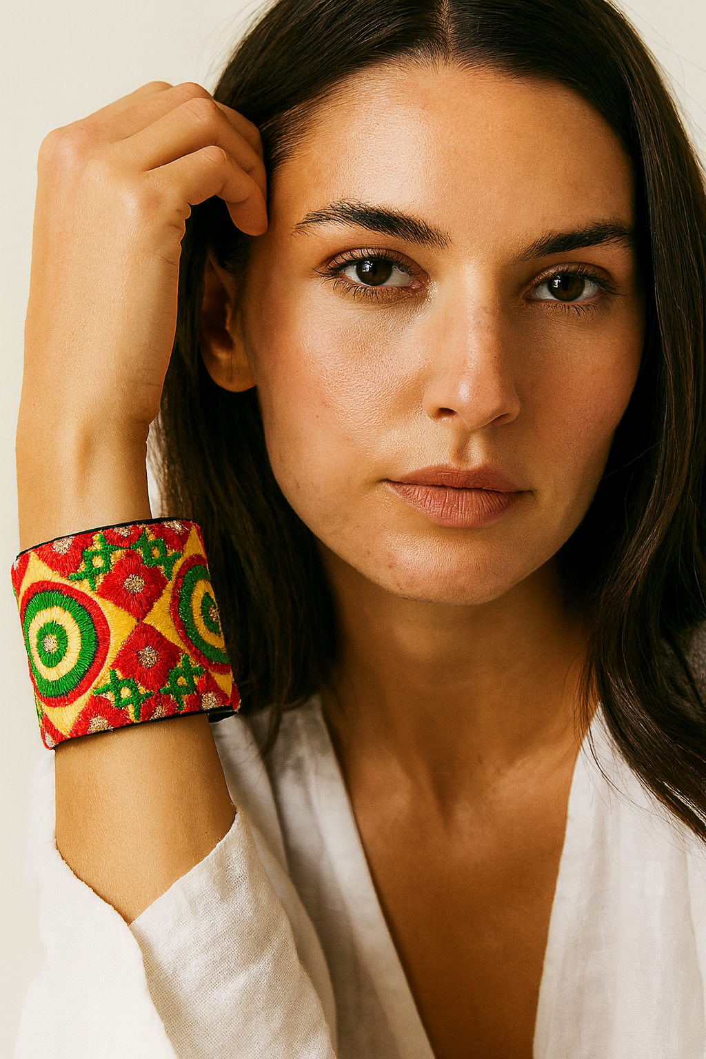 Close-up of a woman wearing the Redd Dott Phoebe 3-inch cuff bracelet, featuring vibrant embroidery in red, green, and yellow with circular and diamond motifs on a bold red base.