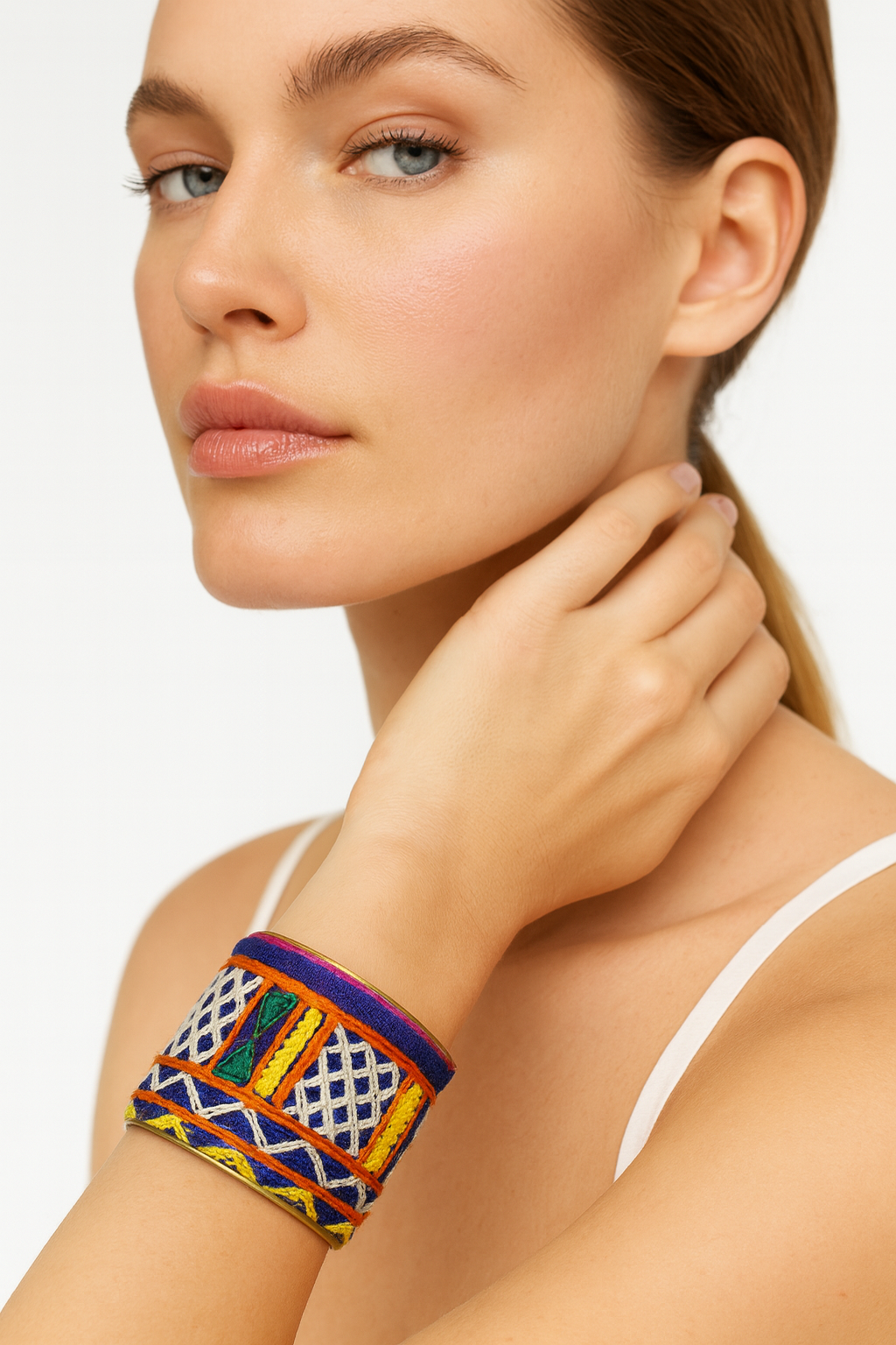Close-up of a woman wearing the Redd Dott Posie 2-inch gold cuff bracelet, featuring bold multicolor geometric embroidery in blue, yellow, green, orange, and white.