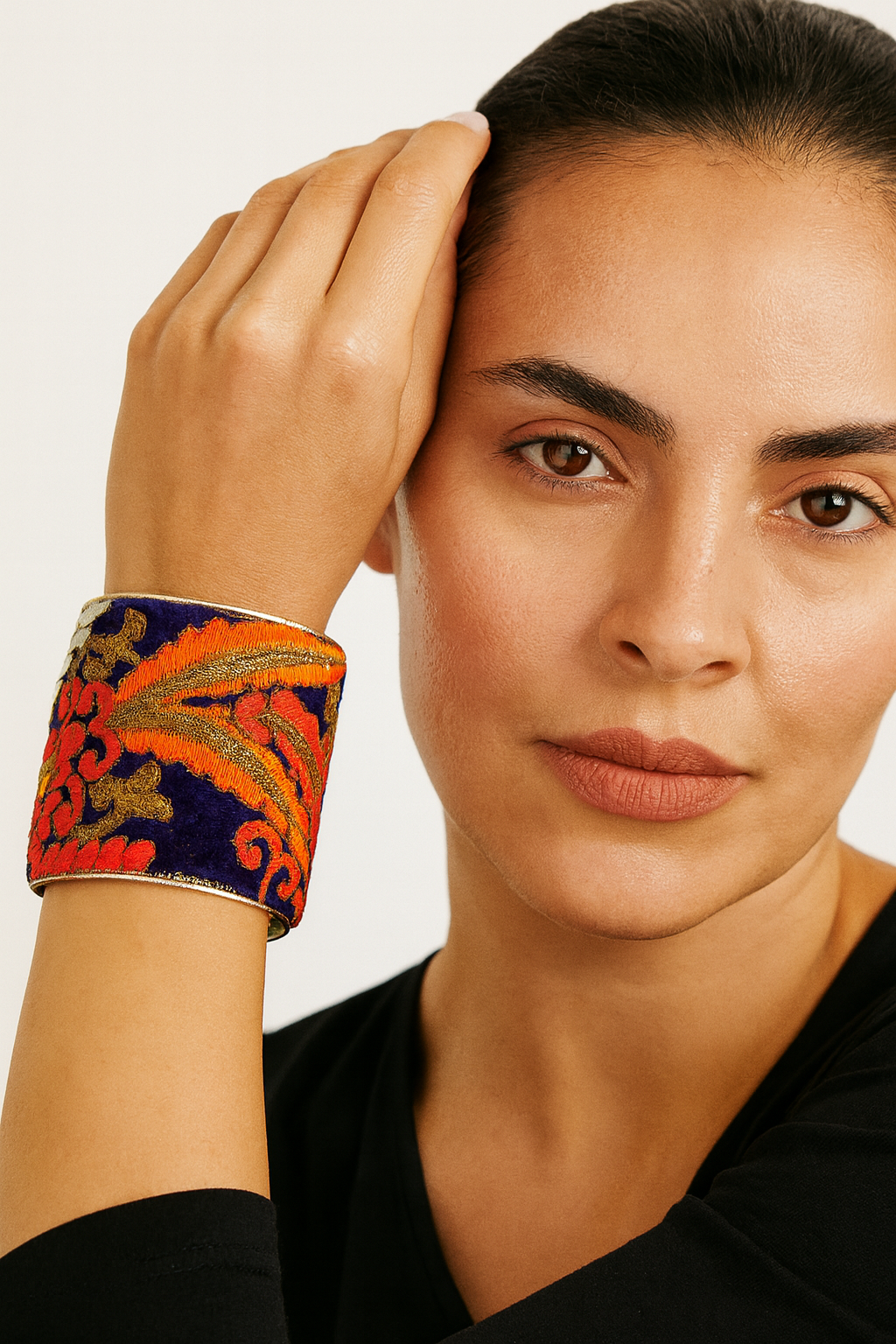 Close-up of a woman wearing the Redd Dott Rasha 3-inch gold cuff bracelet, featuring deep navy fabric with bold red and orange embroidery accented by metallic gold details.