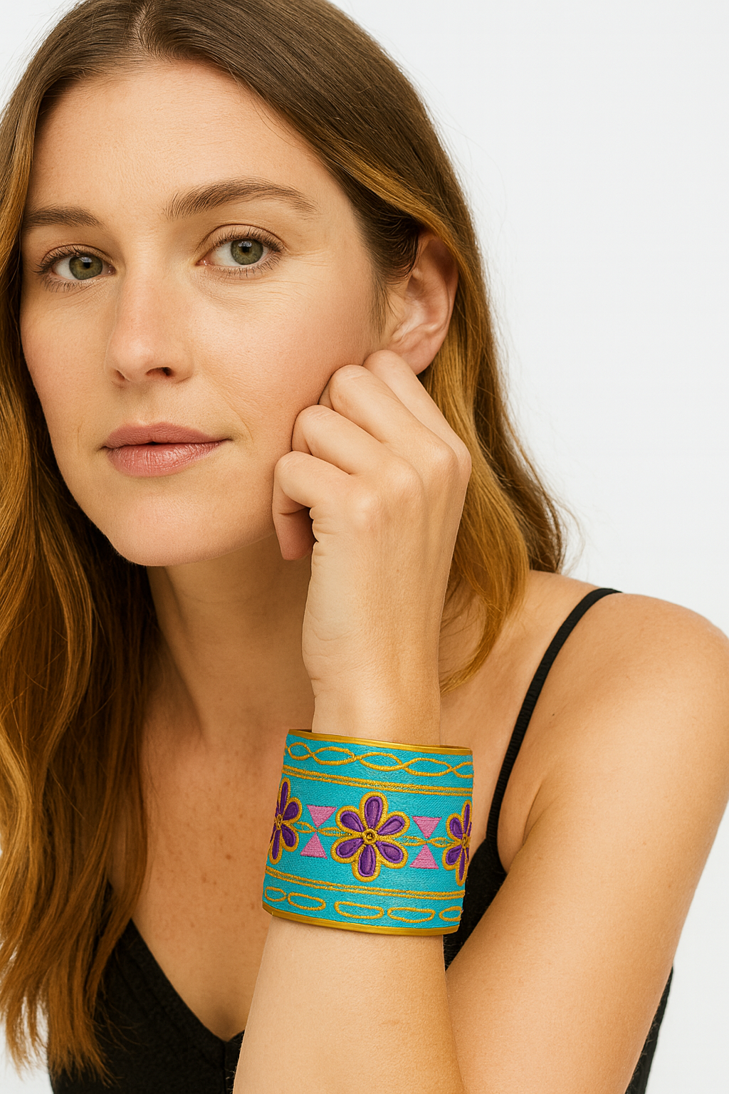 Close-up of a woman wearing the Redd Dott Reah 3-inch gold cuff bracelet, featuring bright turquoise fabric with bold purple embroidered flowers, pink triangle accents, and gold detailing.