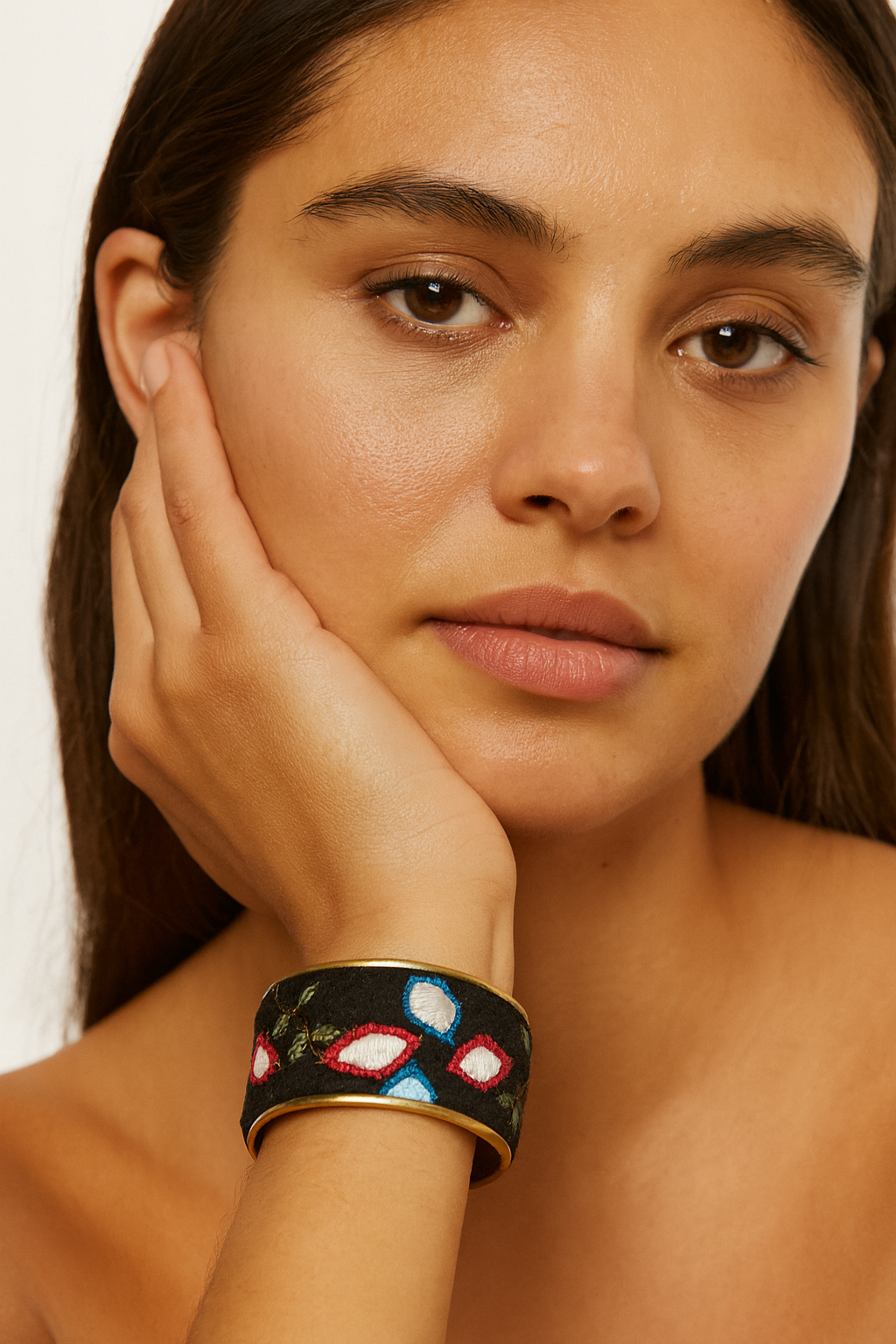 Close-up of a woman wearing the Redd Dott Rina 1-inch gold cuff bracelet, featuring a black fabric base with colorful embroidered petal motifs in red, white, and blue.