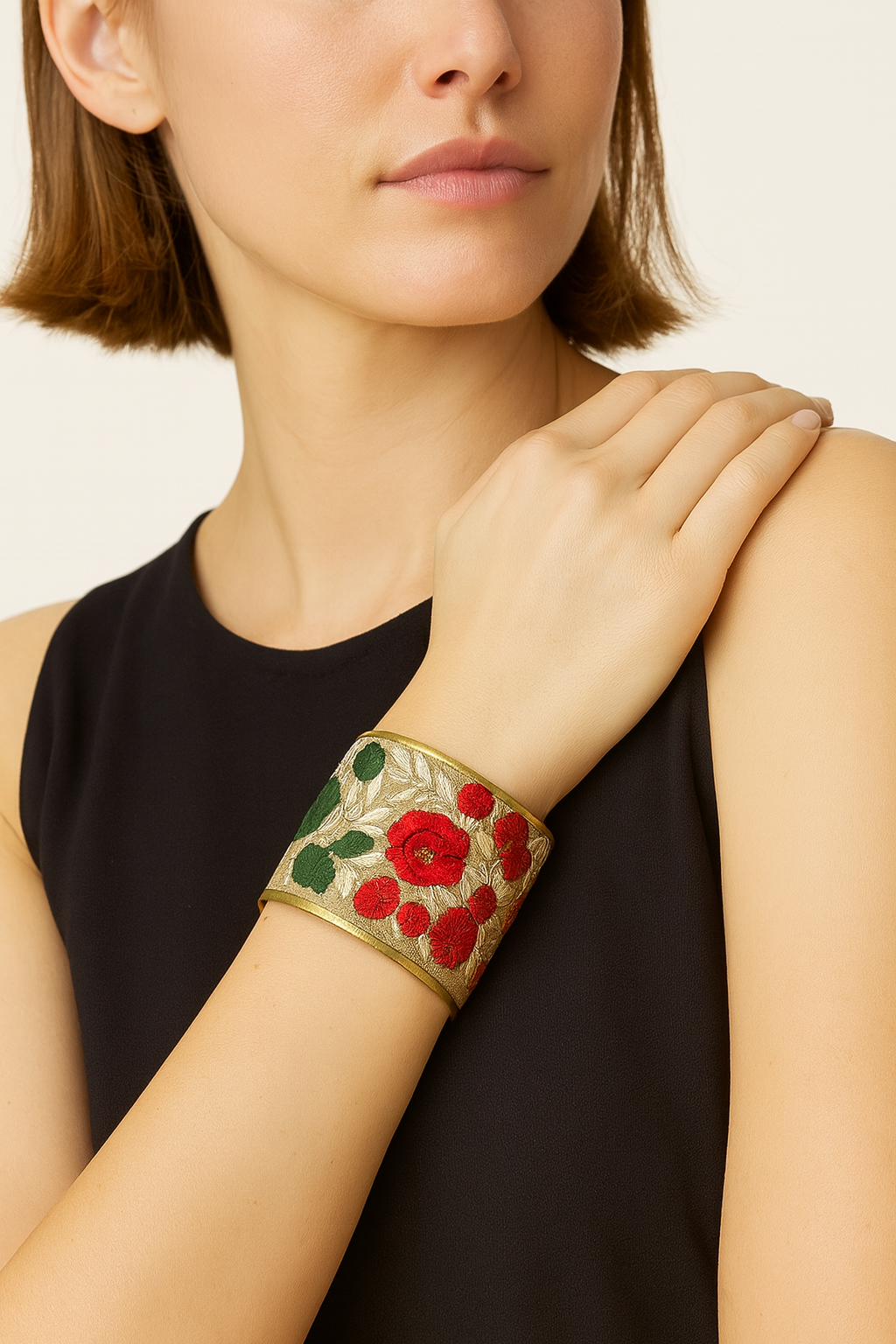 Close-up of a woman wearing a Redd Dott gold cuff bracelet embroidered with vibrant red roses and green leaves, creating an elegant floral statement accessory for special occasions or everyday style.